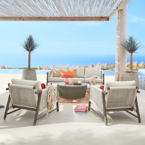 Set di mobili da esterno con cuscini beige e struttura in legno su terrazza con vista mare sotto pergola