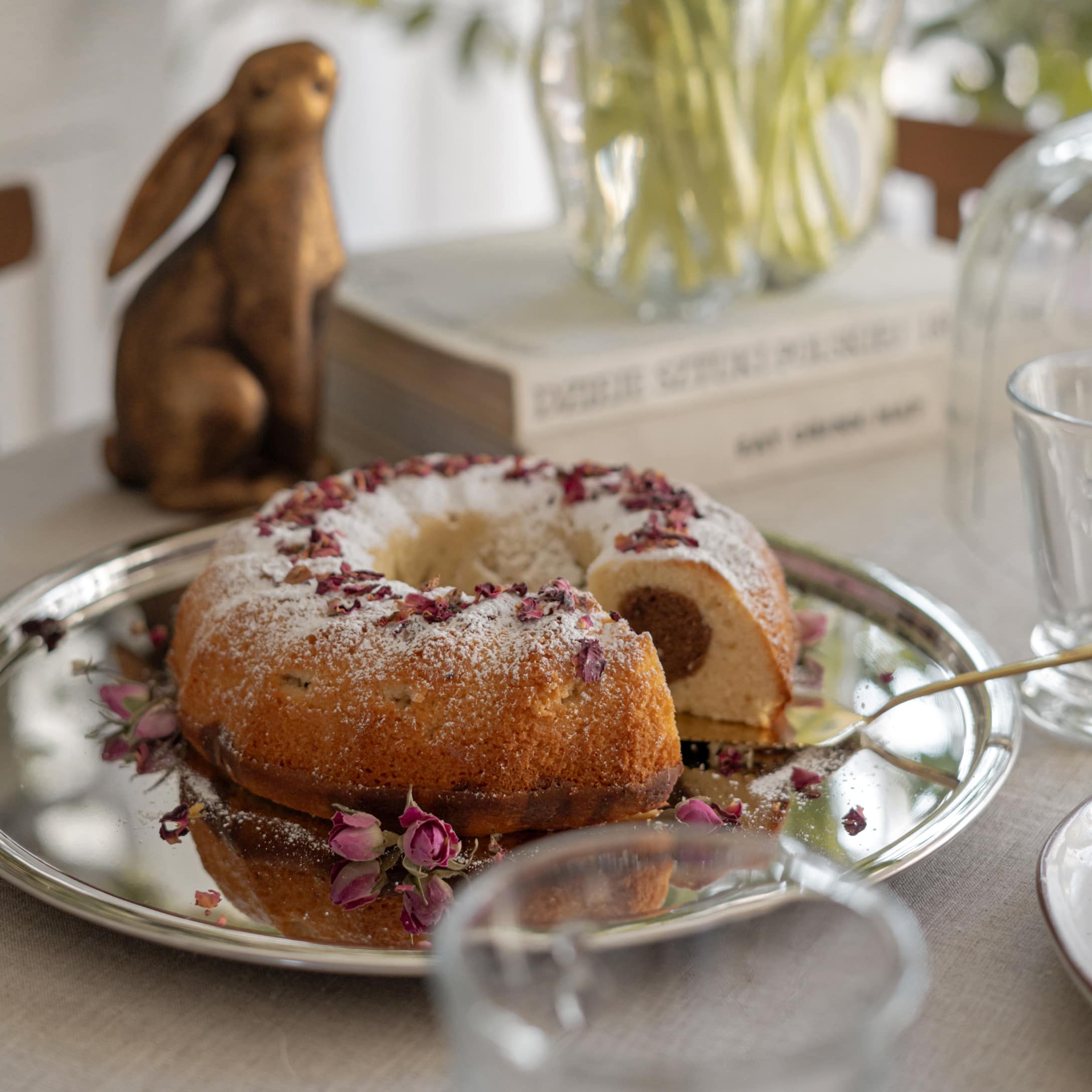 Ciambella con zucchero a velo e petali di rosa secchi su vassoio d'argento sul tavolo