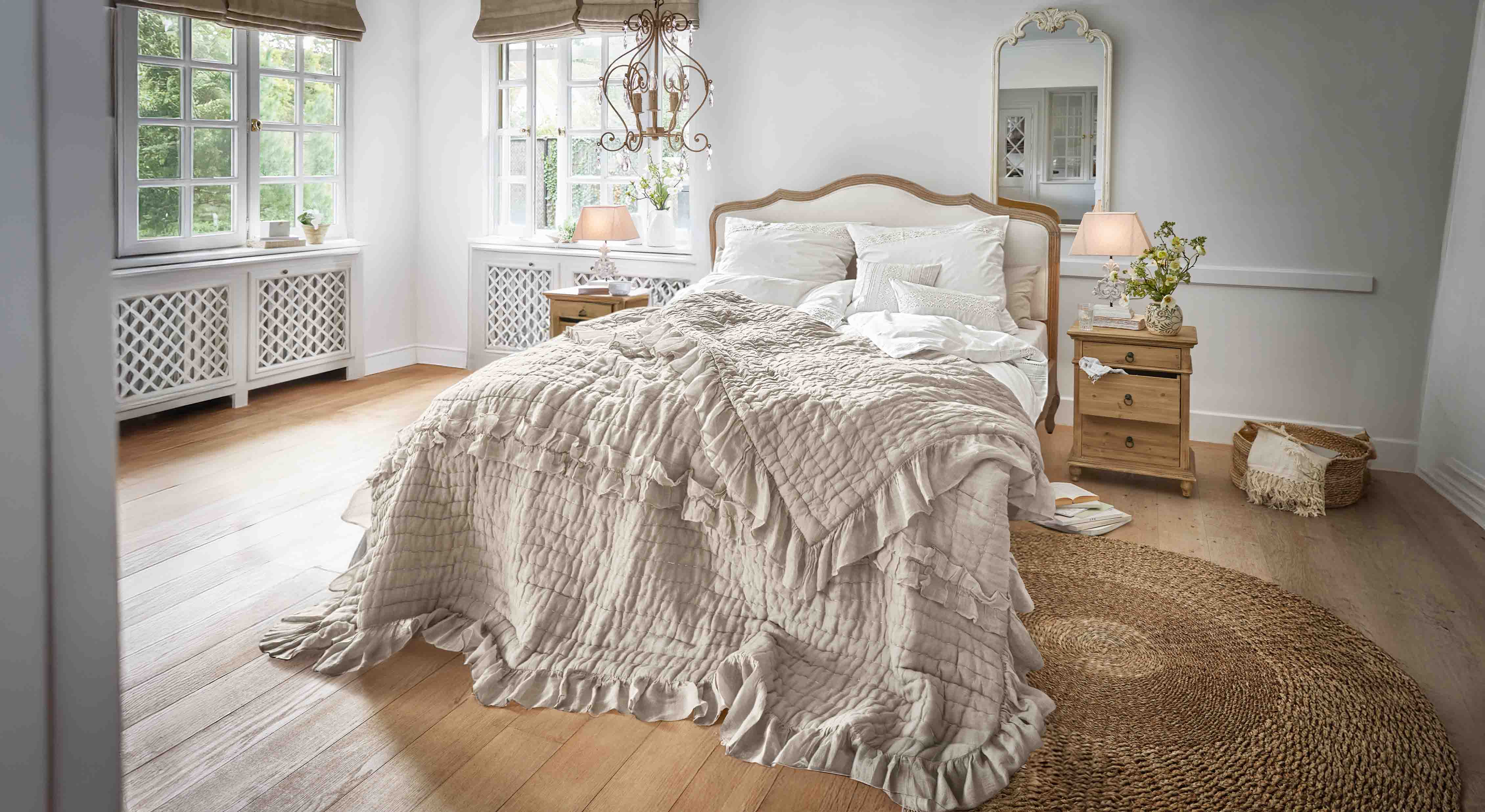 Camera da letto accogliente con letto coperto da trapunta beige con volant e mobili in legno
