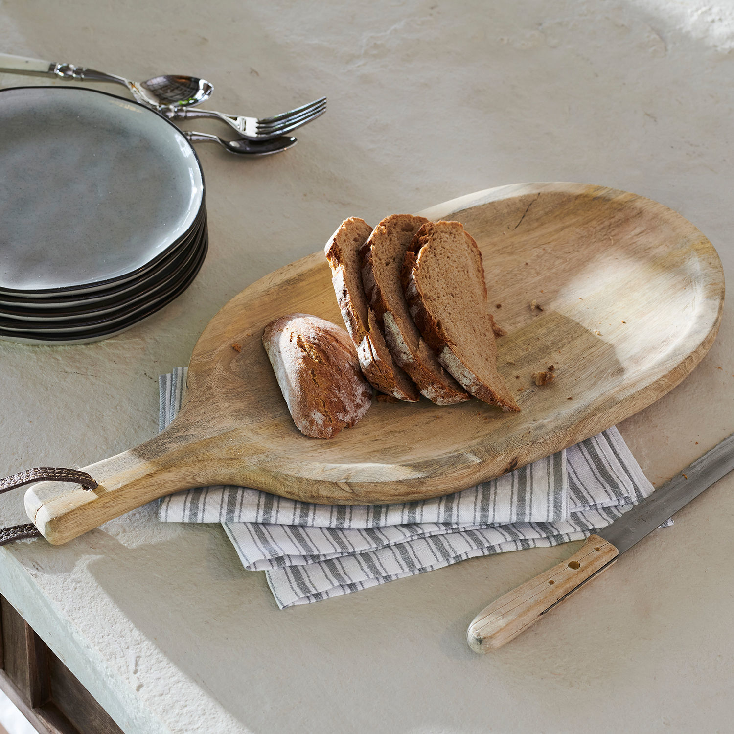 Vassoio Journée Tagliere in legno con manico e fette di pane su piano cucina grigio chiaro