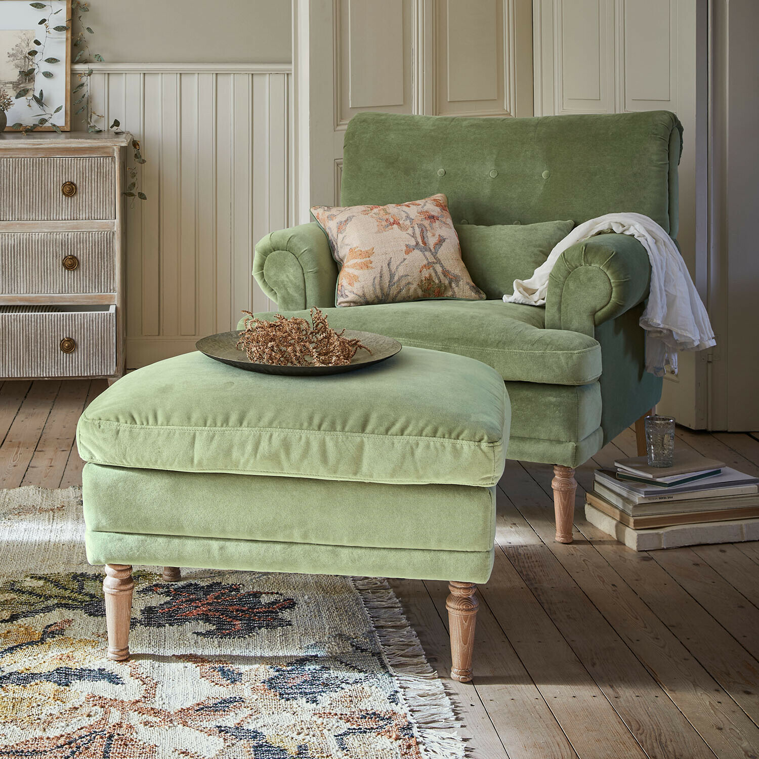 Poltrona verde in velluto con poggiapiedi su gambe in legno in soggiorno accogliente con tappeto