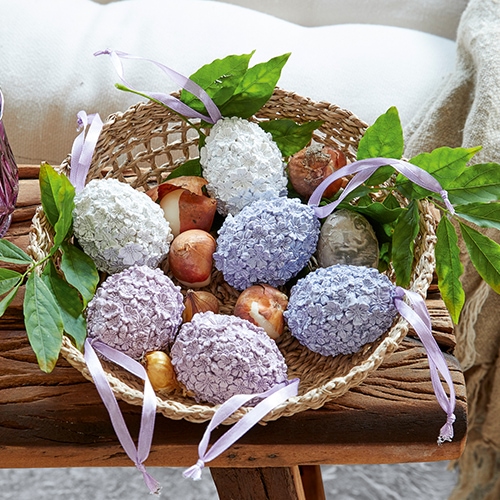 Cesto con uova decorative color pastello e foglie verdi su tavolo in legno rustico