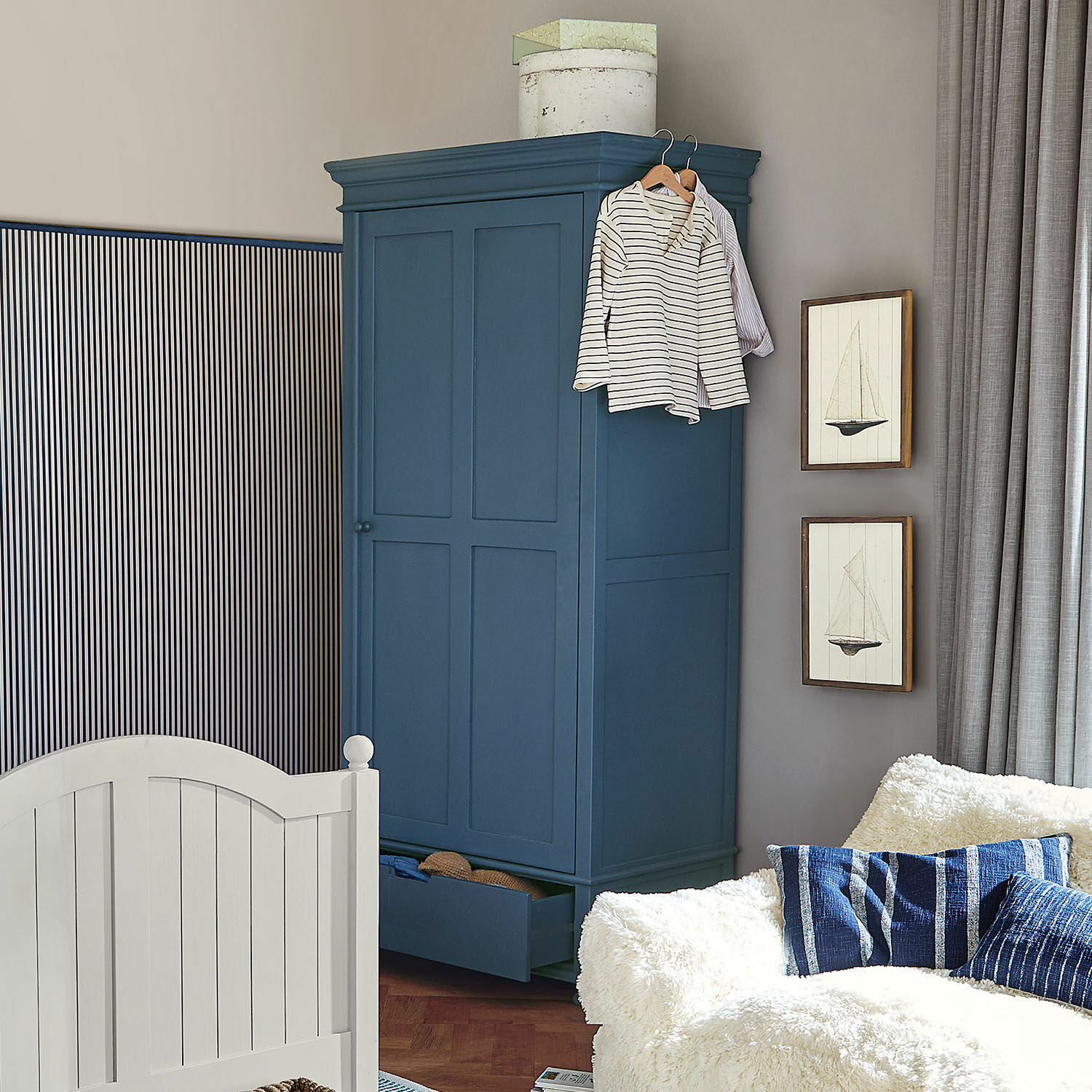 Armadio Westcombe Armadio in legno blu navy con cassetto aperto e abiti appesi in soggiorno accogliente con divano bianco