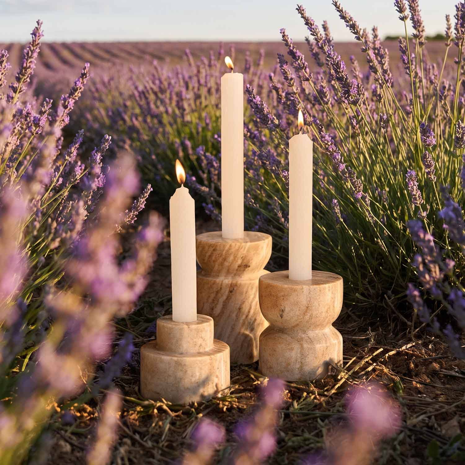 Tre candele crema in portacandele di legno naturale in un campo di lavanda al tramonto