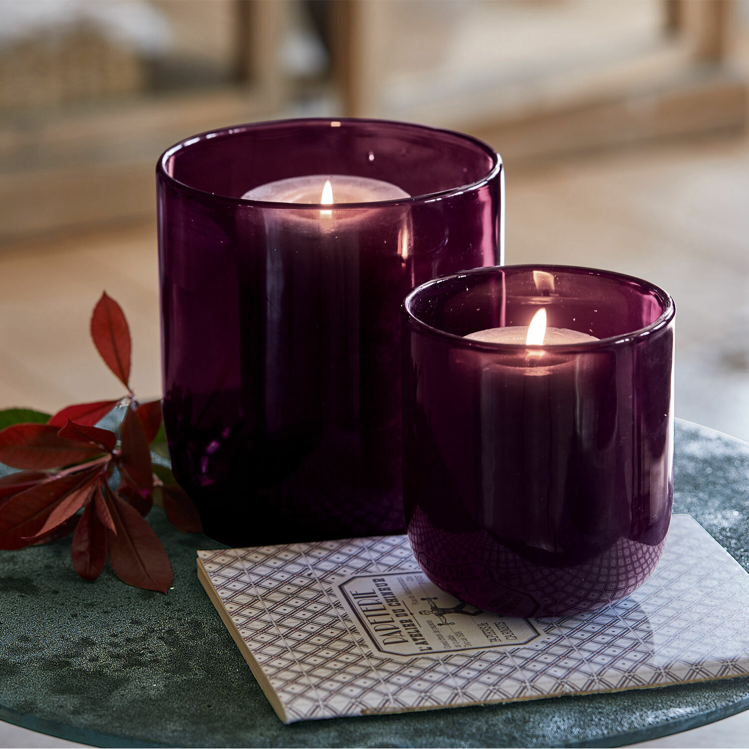 Coppia di portacandele Theodor Due lanterne in vetro viola con candele accese su un sottopentola decorativo su tavolo verde