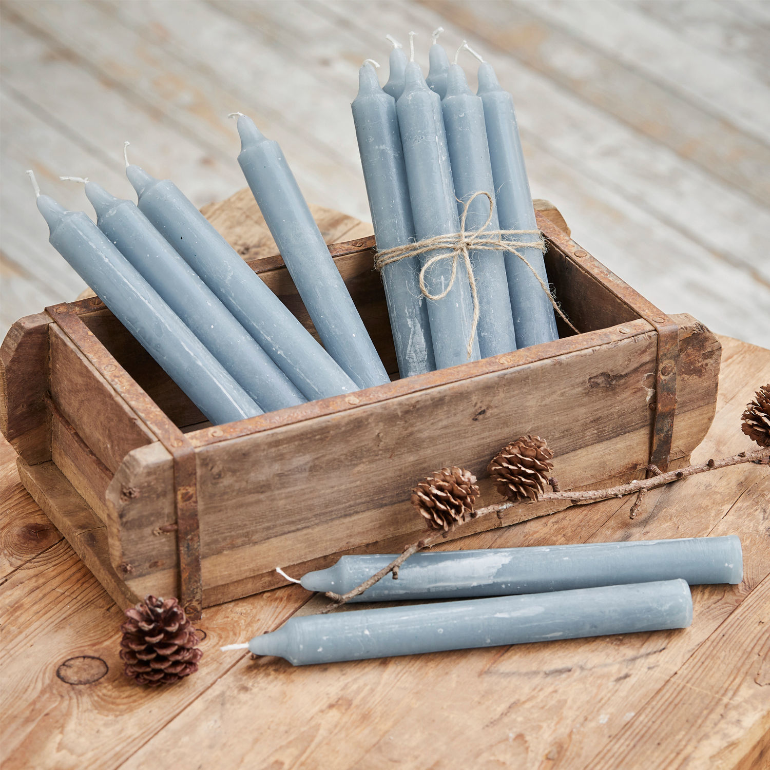 Set di 12 candele Bauceau Set di candele blu in cera in scatola di legno su tavolo rustico con pigne