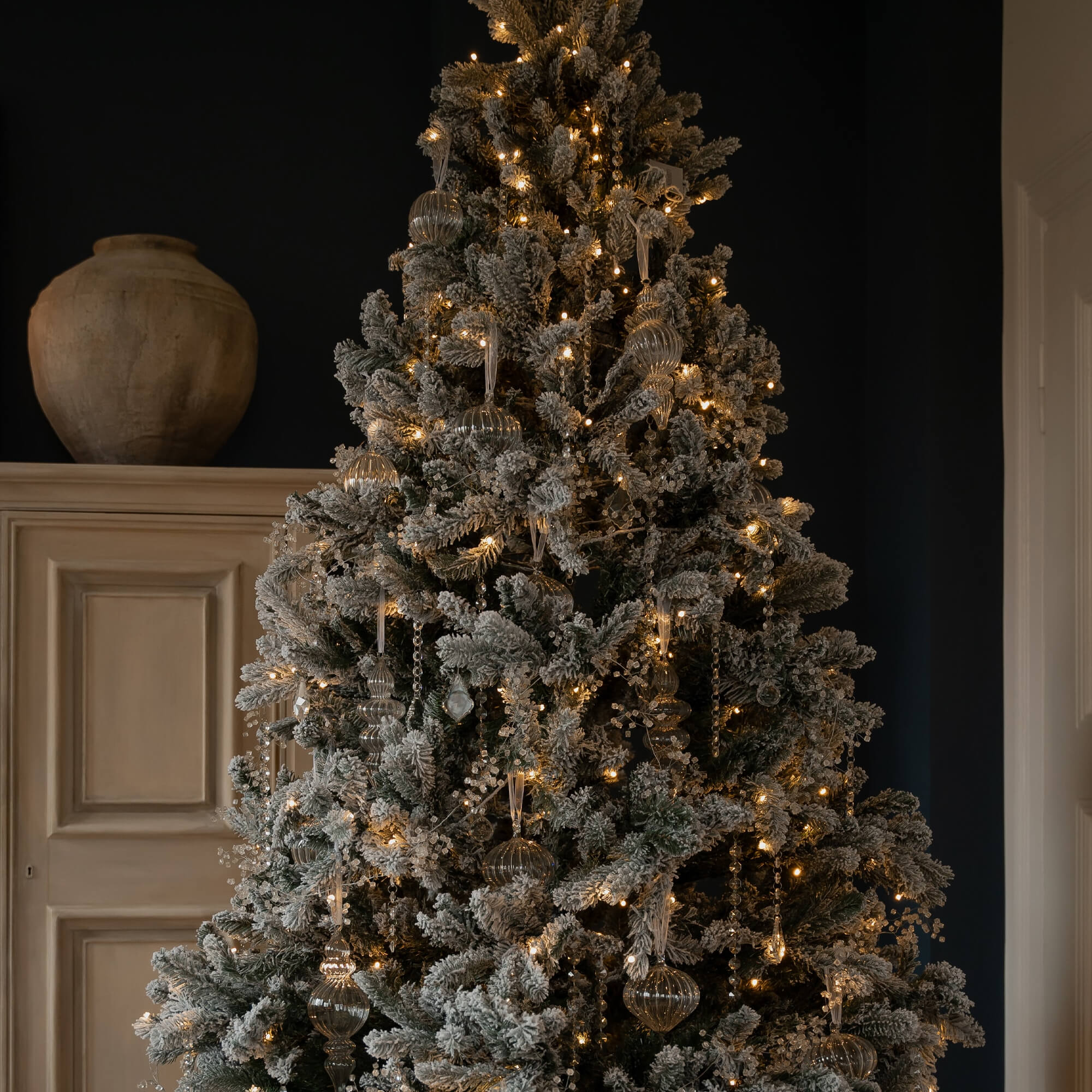 Albero di Natale innevato con decorazioni trasparenti e luci calde in un ambiente elegante