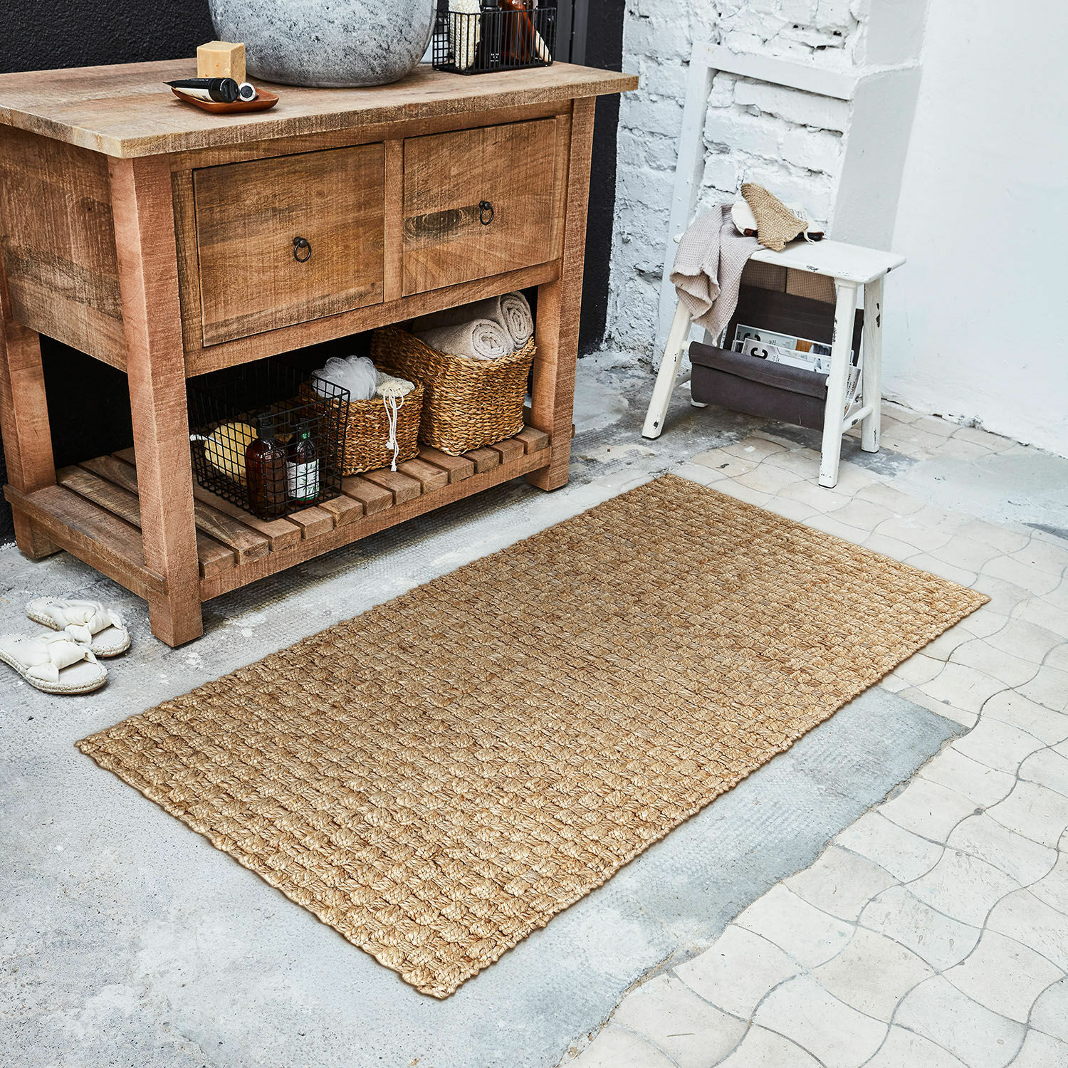 Passatoia Daoukro Tappeto beige in juta naturale sul pavimento accanto a un mobile in legno e uno sgabello bianco