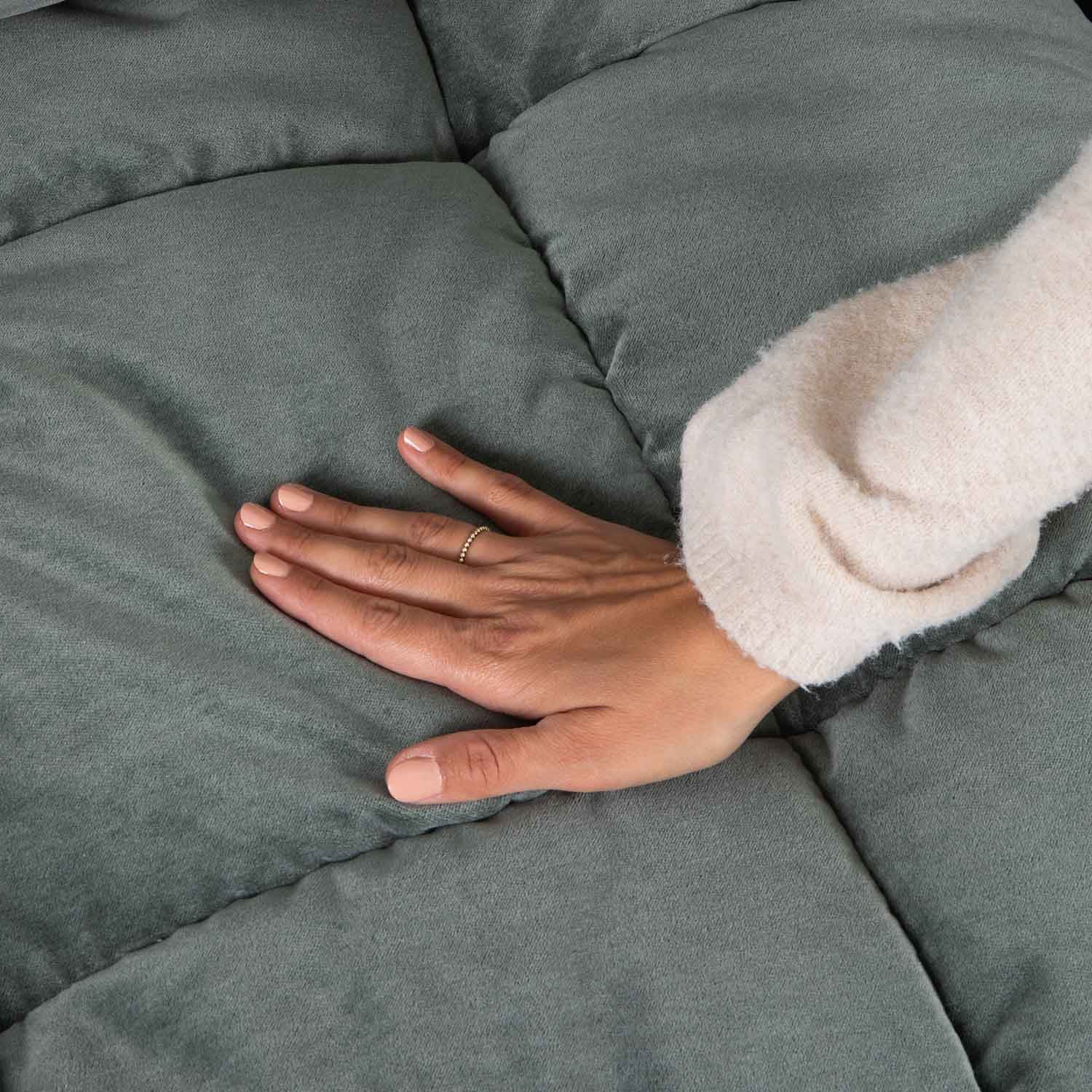 Mano su tessuto trapuntato verde morbido, che evidenzia comfort e qualità del materiale