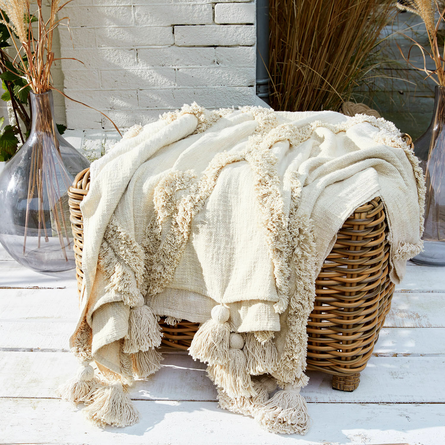 Coperta Linares Coperta crema in cotone con nappine su cesta in vimini, decorazione e comfort