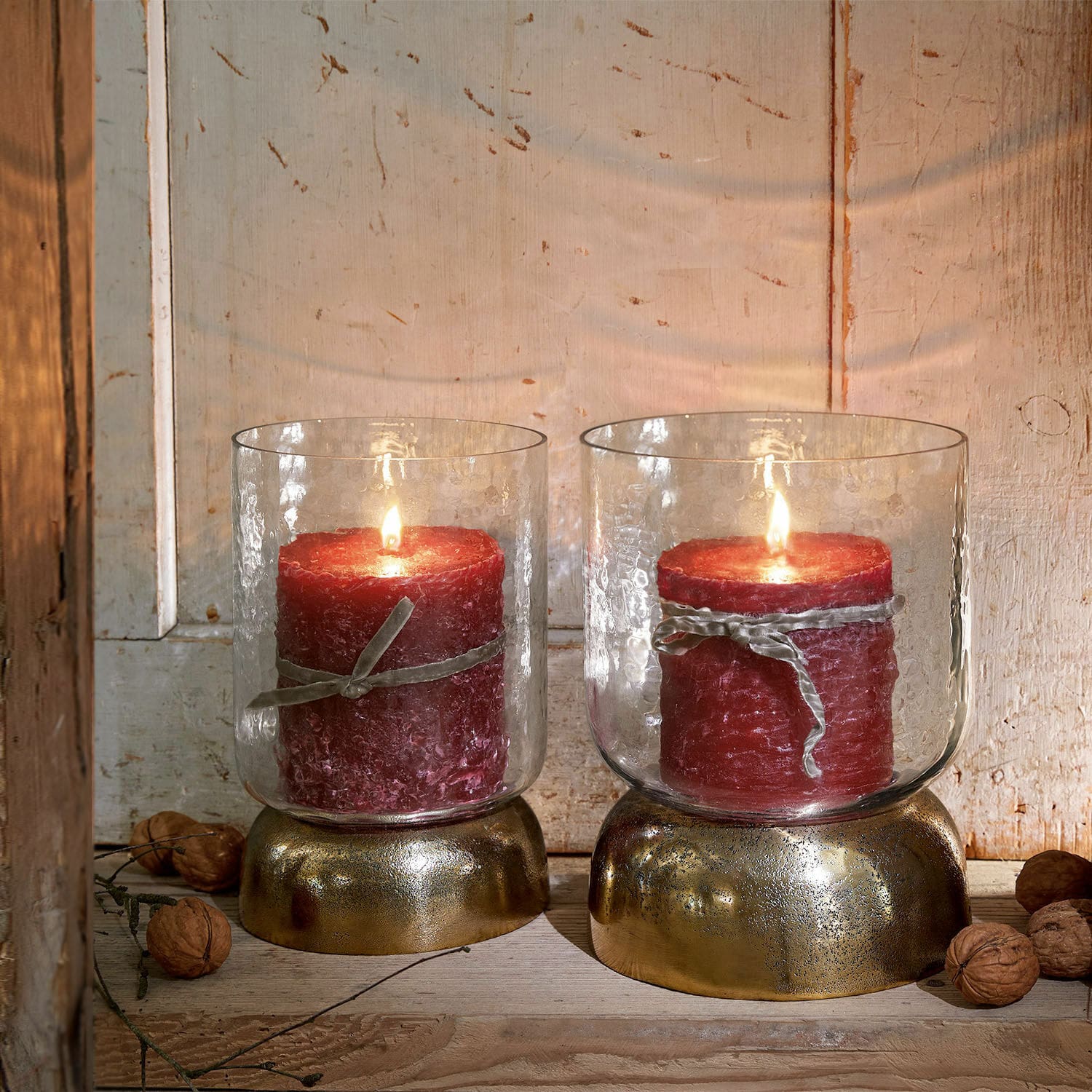 Coppia di portacandele Biserre Due candele rosse in contenitori di vetro con base dorata su sfondo di legno rustico