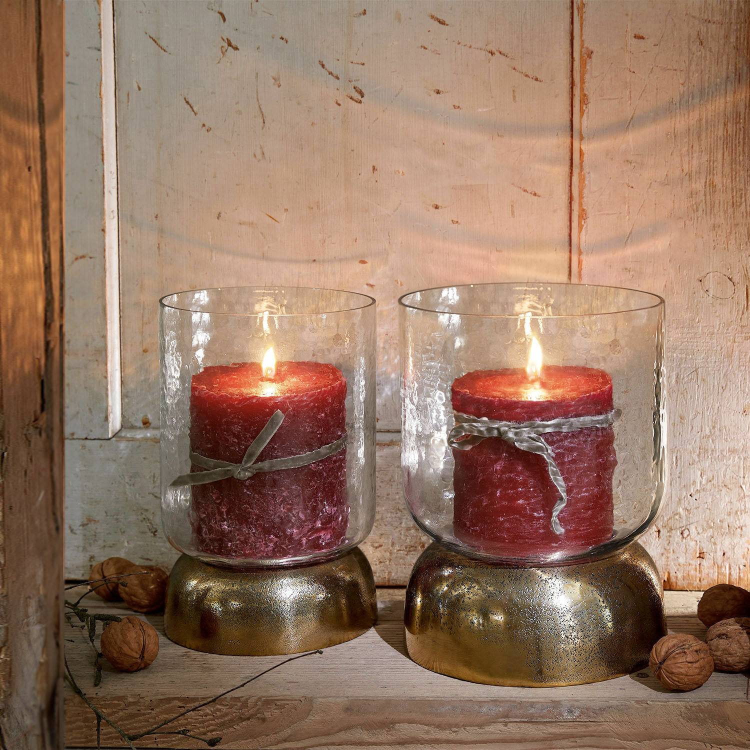 Coppia di portacandele Biserre Due candele rosse in contenitori di vetro con base dorata su sfondo di legno rustico