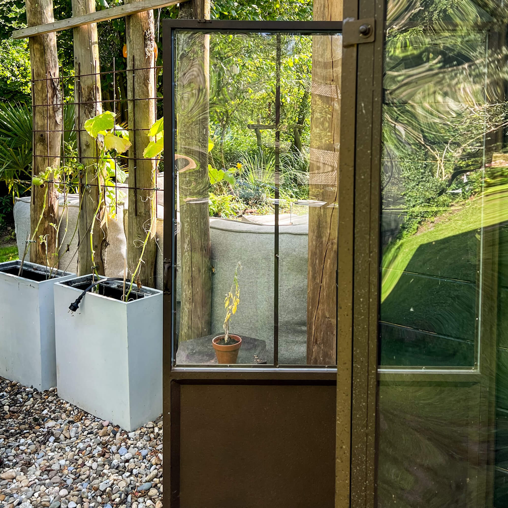 Porta da giardino in vetro con cornice metallica davanti a piante in vaso e ciottoli