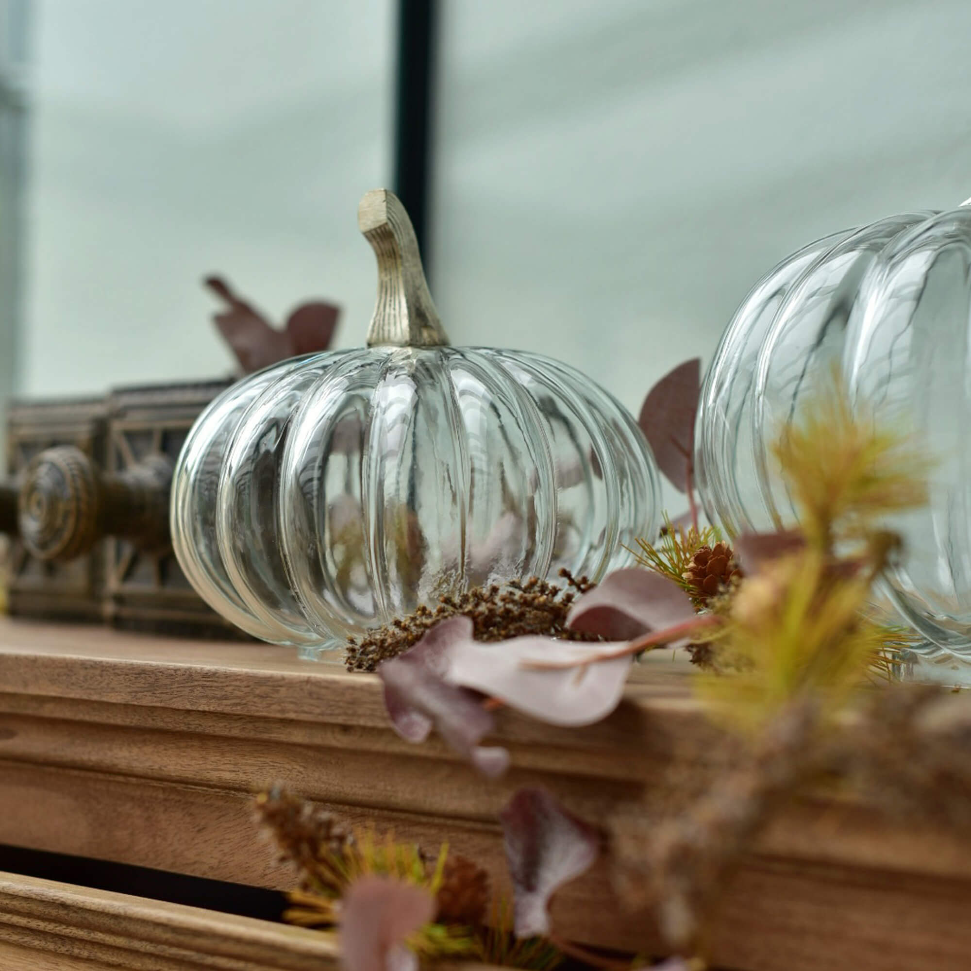 Zucca in vetro trasparente con gambo beige su piano in legno con decorazioni autunnali