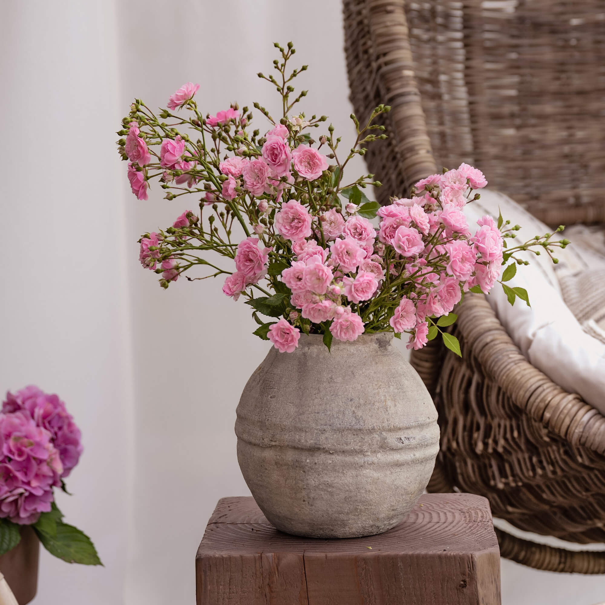 Vaso in ceramica grigia con fiori rosa su tavolo di legno in ambiente accogliente