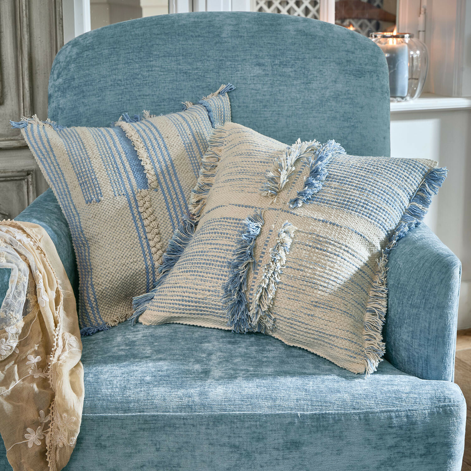 Coppia di copricuscini Ciel d'Azur Due cuscini decorativi in cotone crema e blu su una poltrona morbida blu in soggiorno luminoso