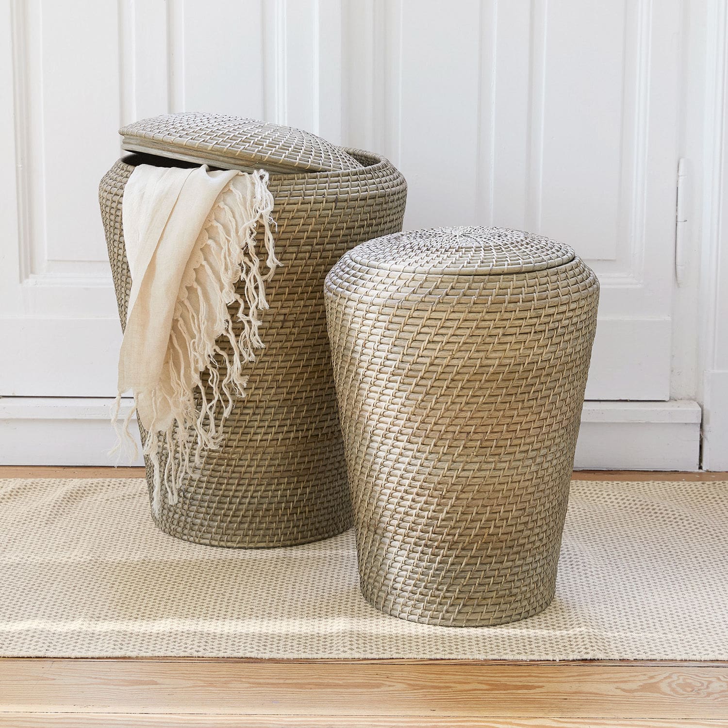 Coppia di cesti portabiancheria Nora Due cesti in rattan beige con coperchi su tappeto, contenitori pratici per la casa