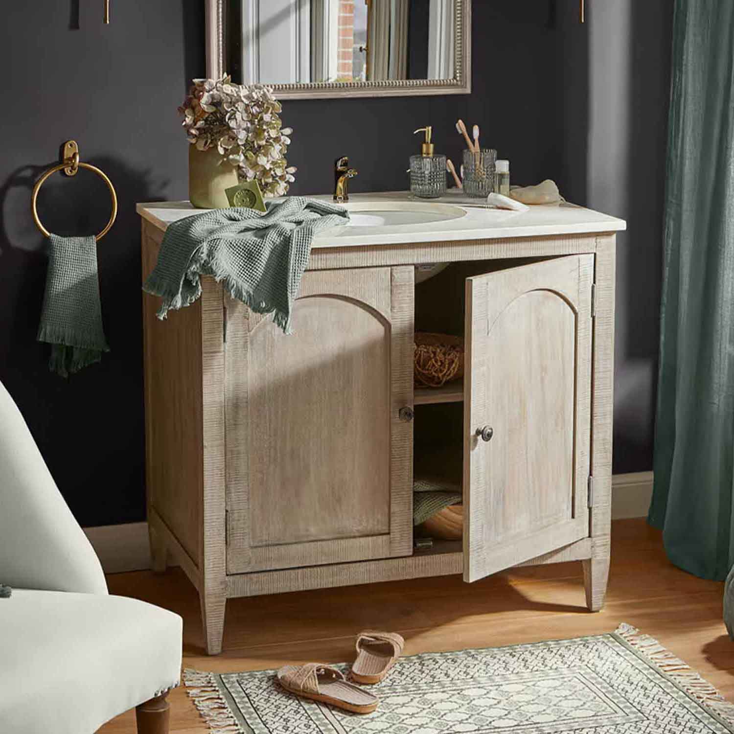 Mobile bagno in legno chiaro con lavabo bianco e rubinetto dorato, asciugamani verdi e decorazioni