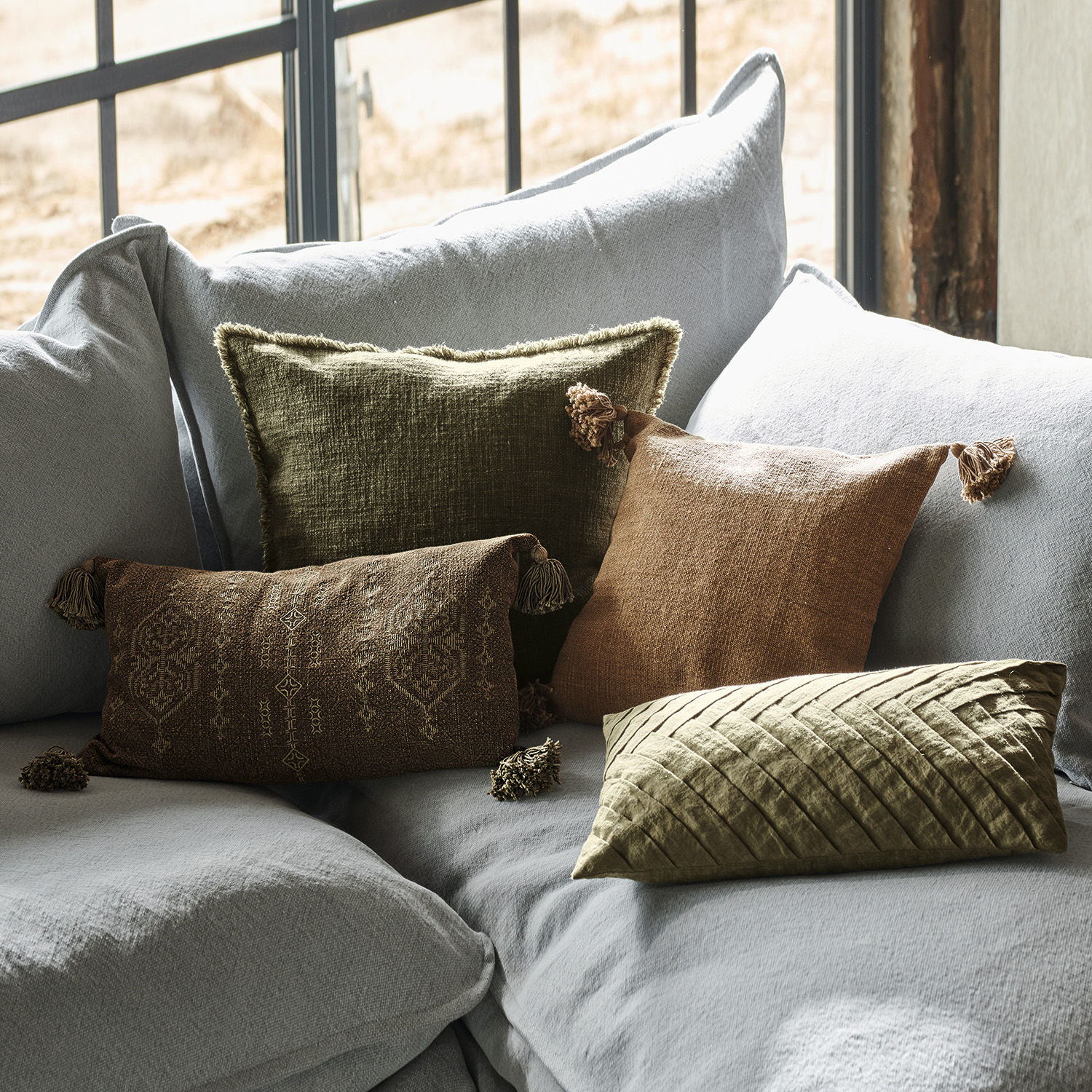Set di 4 copricuscini Donagh Set di cuscini decorativi in tessuto marrone e verde su divano grigio chiaro