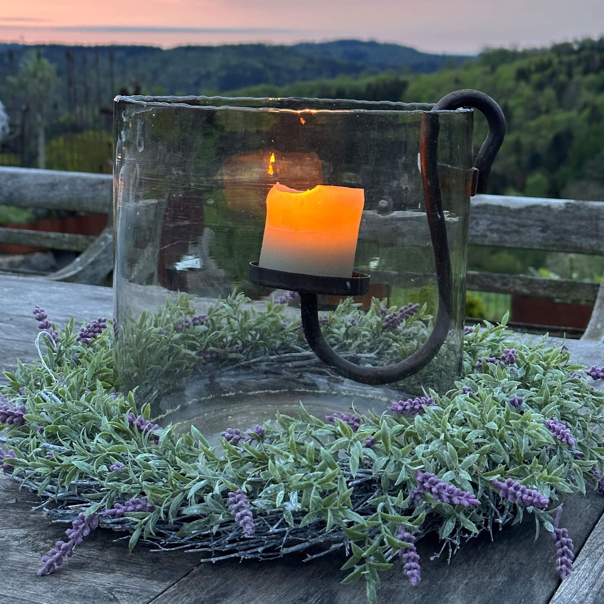 Portacandela in vetro con supporto in metallo e corona verde con fiori viola su tavolo in legno