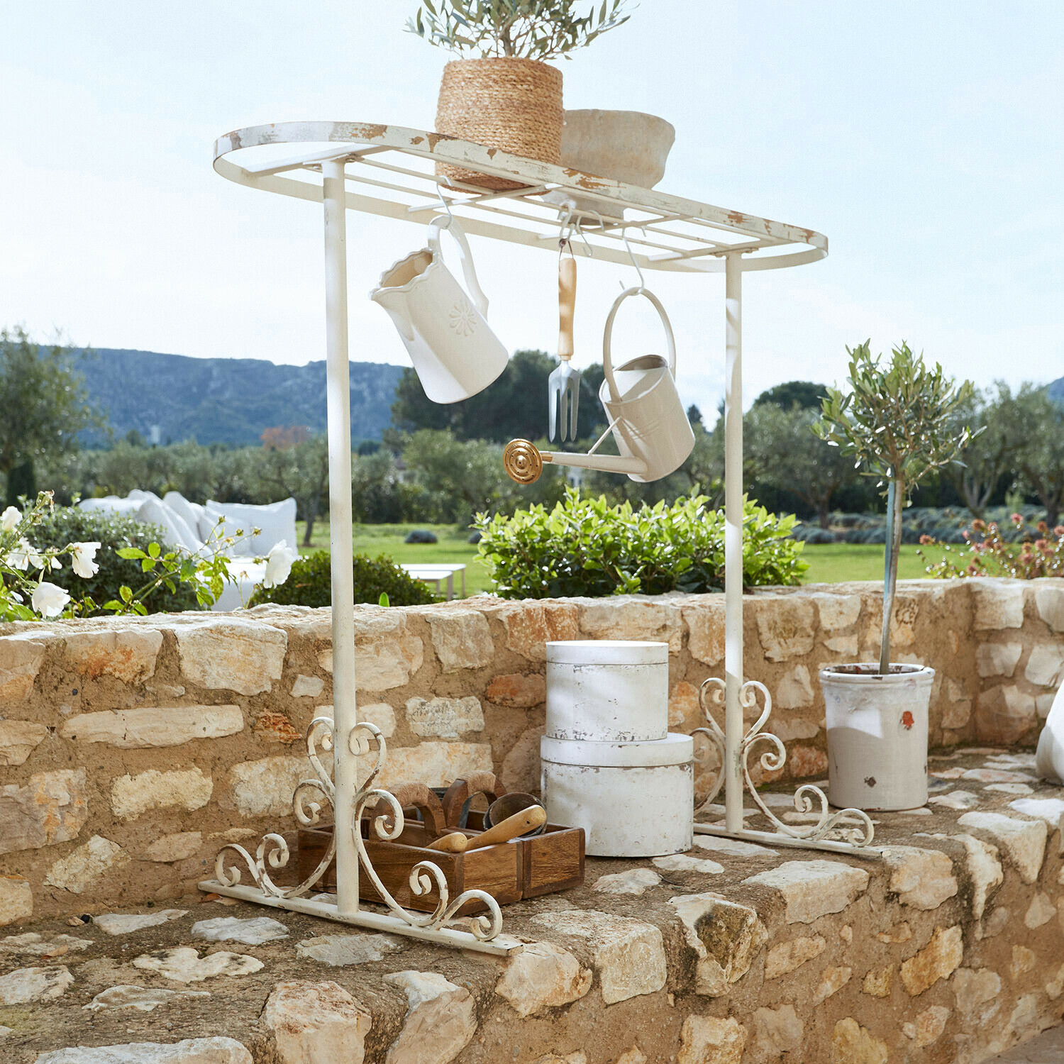 Supporto per tavolo per piante Mairoux Mensola da giardino in metallo bianco con accessori appesi e vaso su muro di pietra in giardino