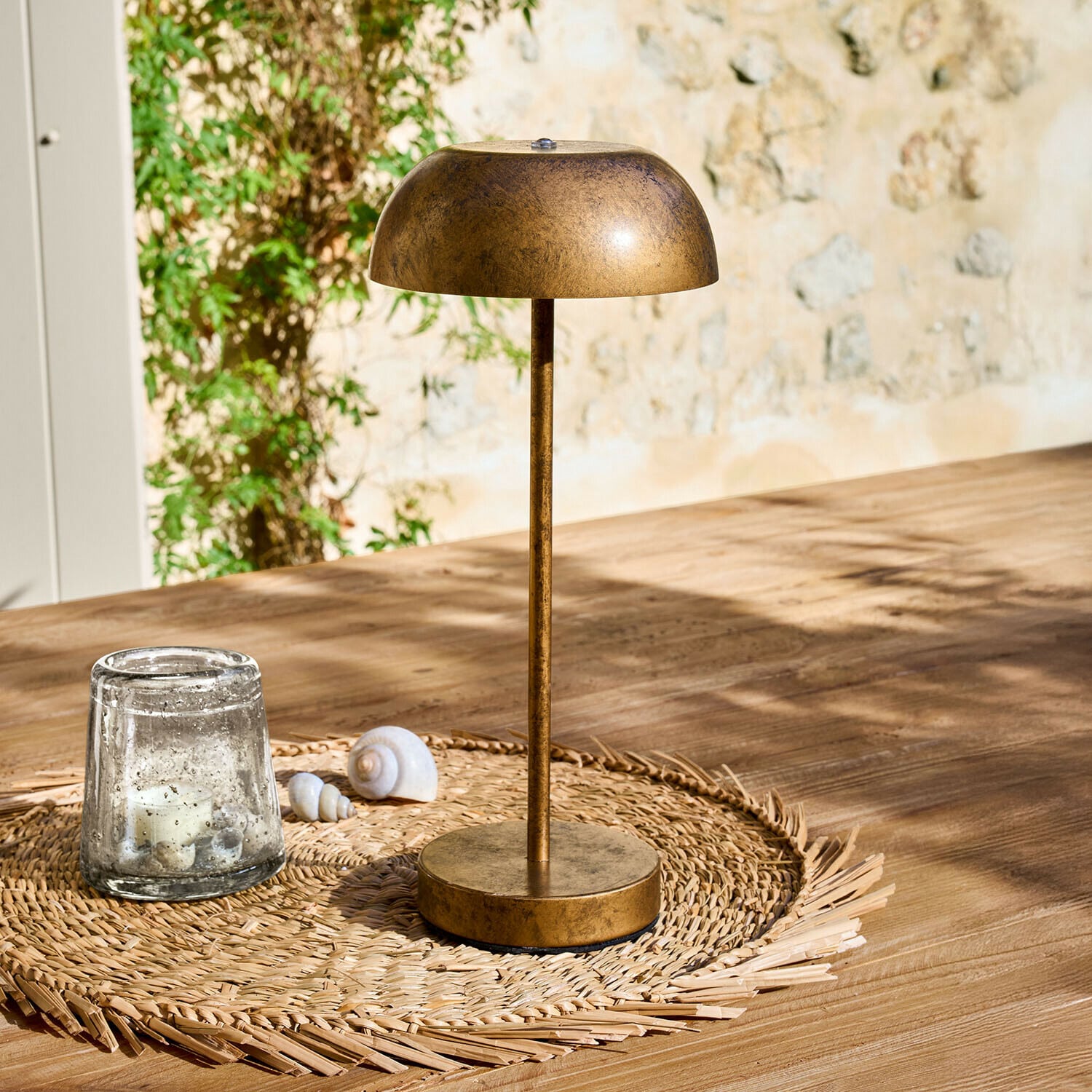 Lampada da tavolo ricaricabile Lumirah Lampada da tavolo in metallo color oro antico su sottopentola intrecciato su tavolo in legno