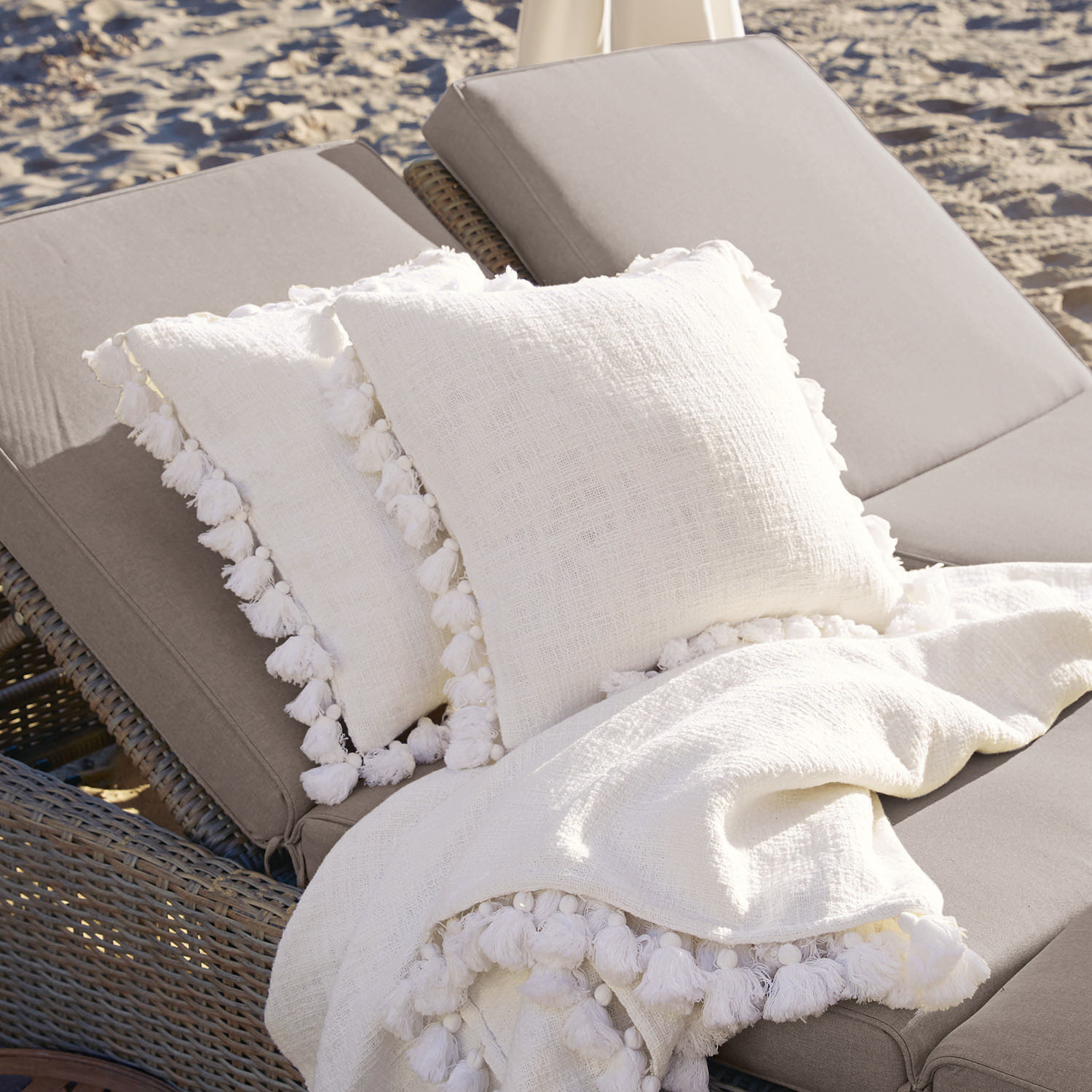 Coppia di copricuscini Peniel Cuscini e coperta bianchi in lino con nappine su lettino grigio in spiaggia