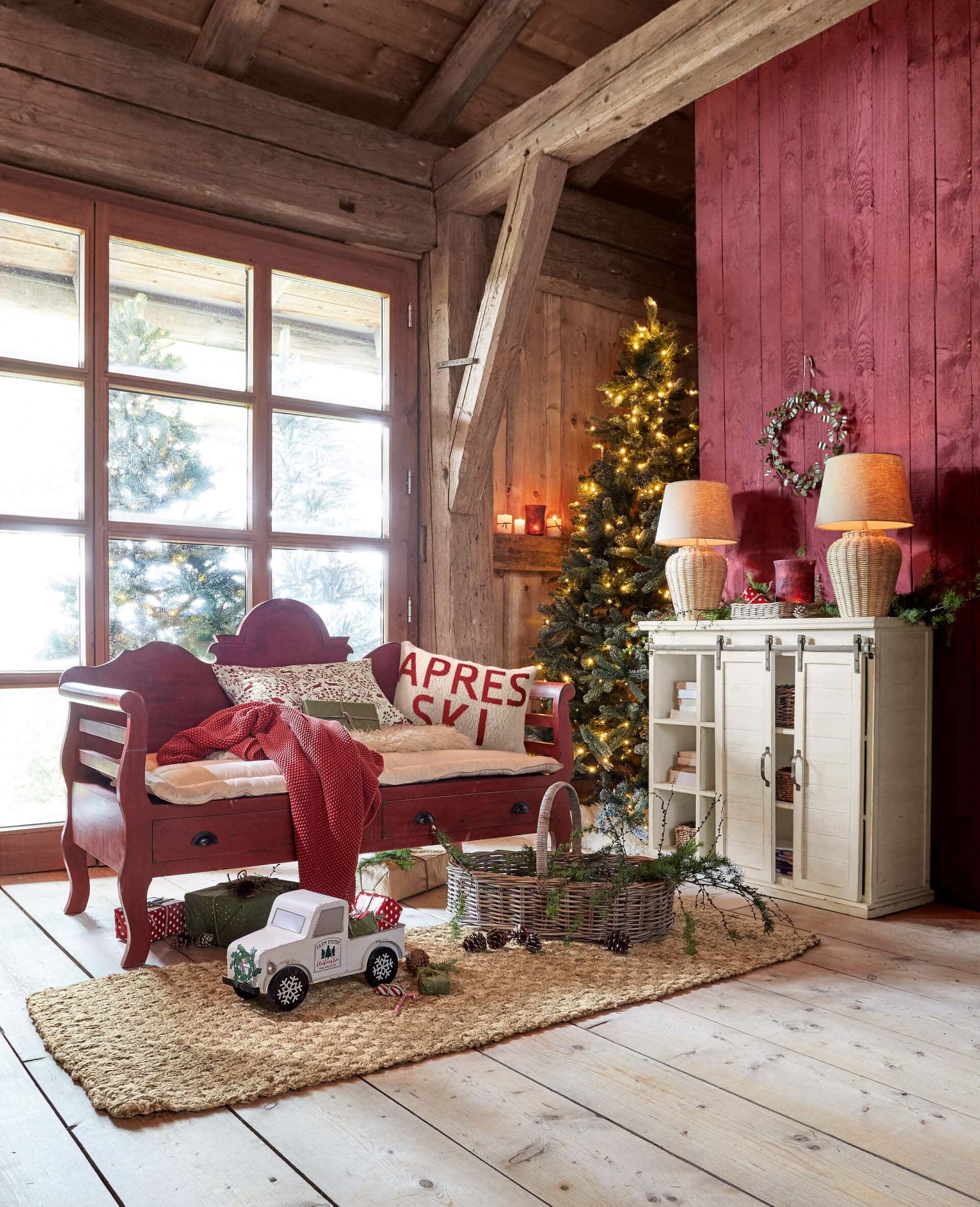 Soggiorno accogliente con panca in legno rossa, albero di Natale illuminato e decorazioni su tappeto di juta