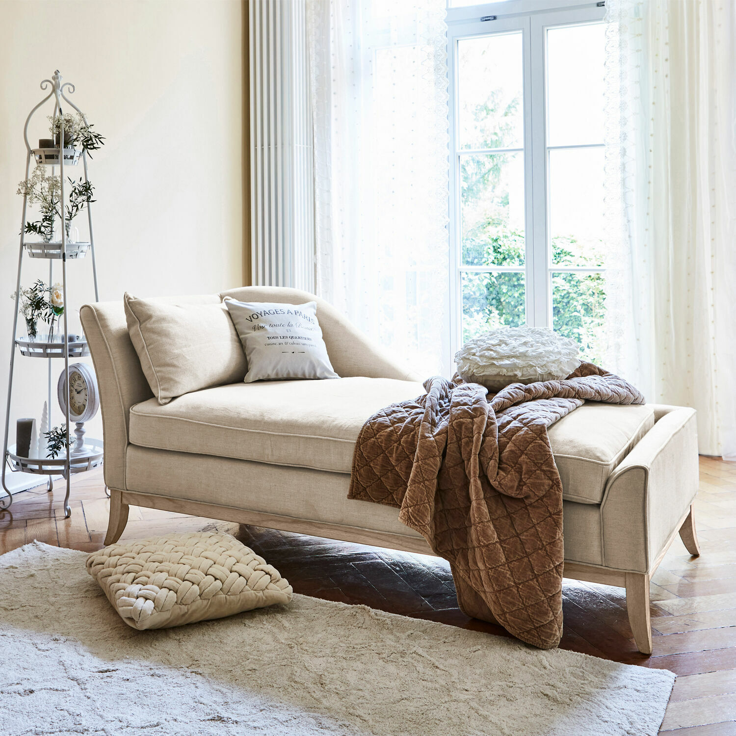 Chaise longue Alphonse Chaise longue beige in tessuto con cuscini e coperta marrone in soggiorno luminoso
