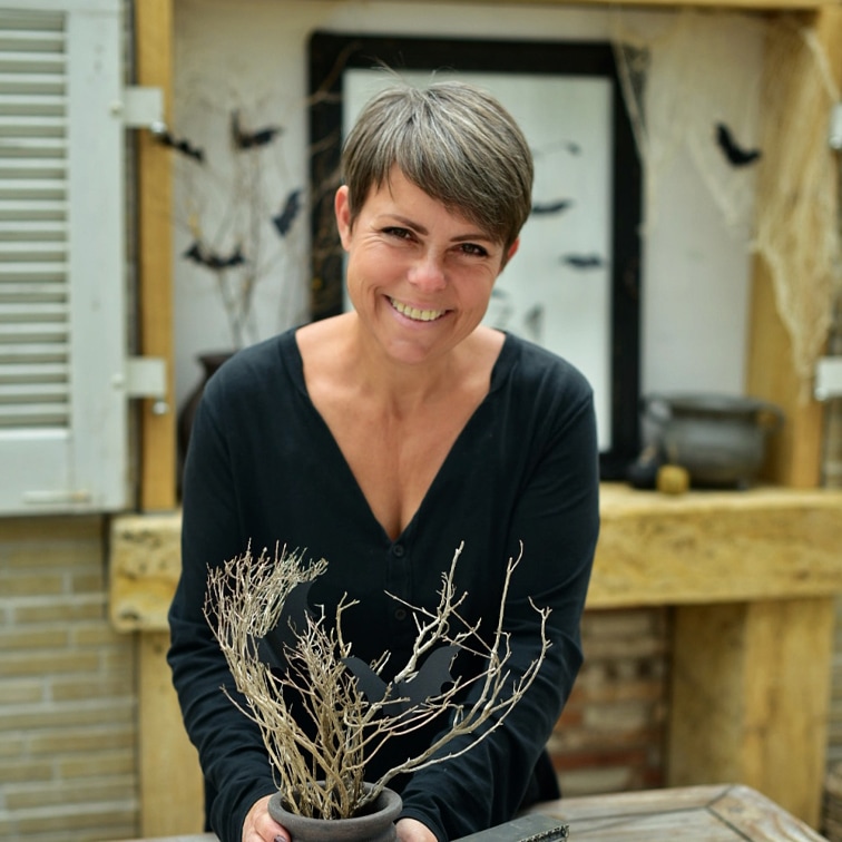 Donna con maglia nera tiene vaso con rami secchi e decorazioni di pipistrelli in ambiente rustico