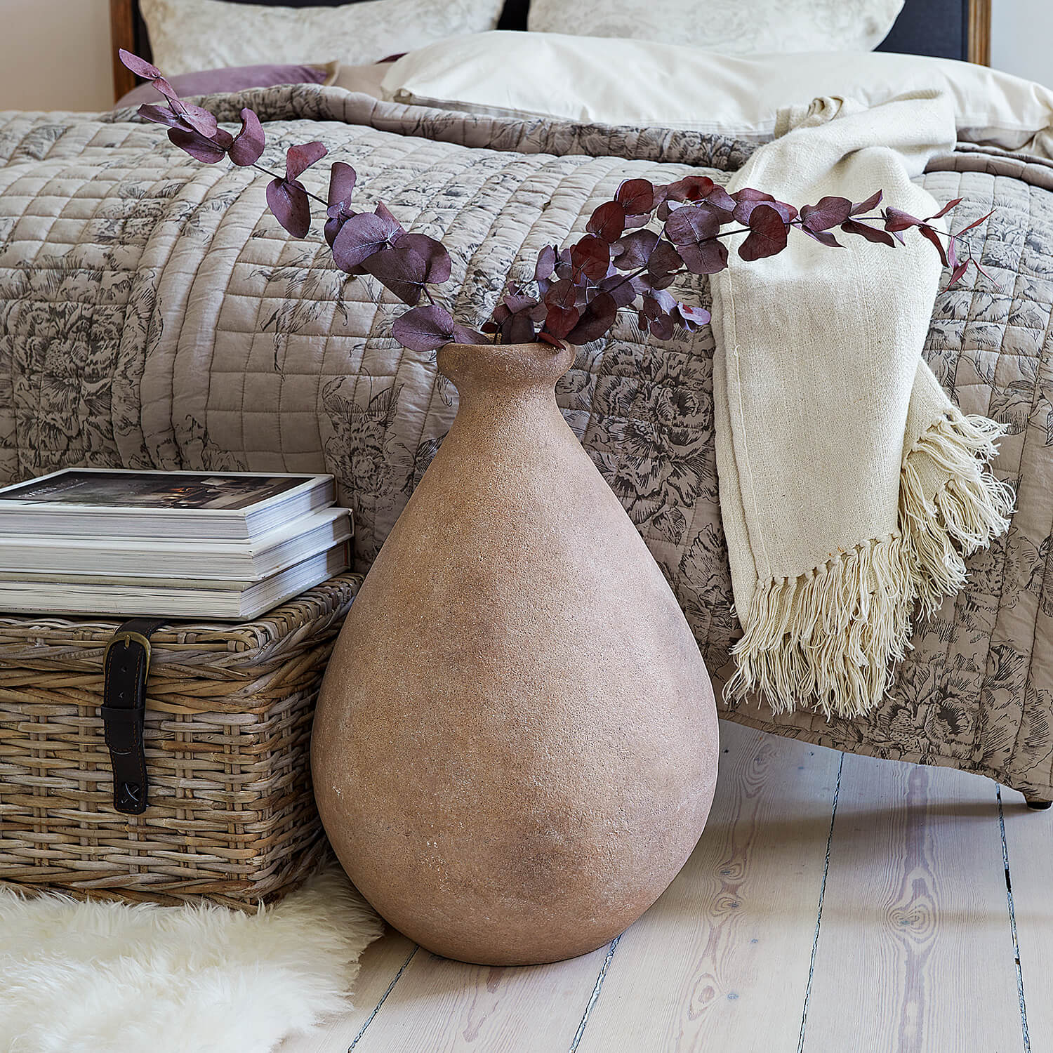 Grande vaso in ceramica beige con rami secchi davanti a letto e cesto in vimini