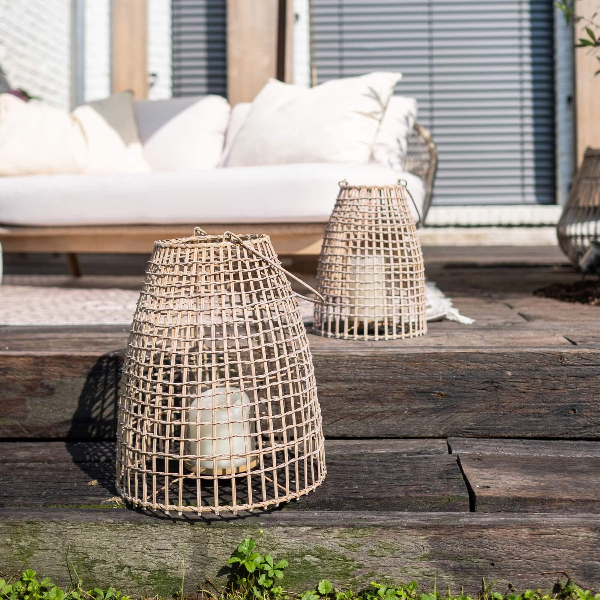 Lanterna in vimini naturale con candela bianca su terrazza in legno rustico
