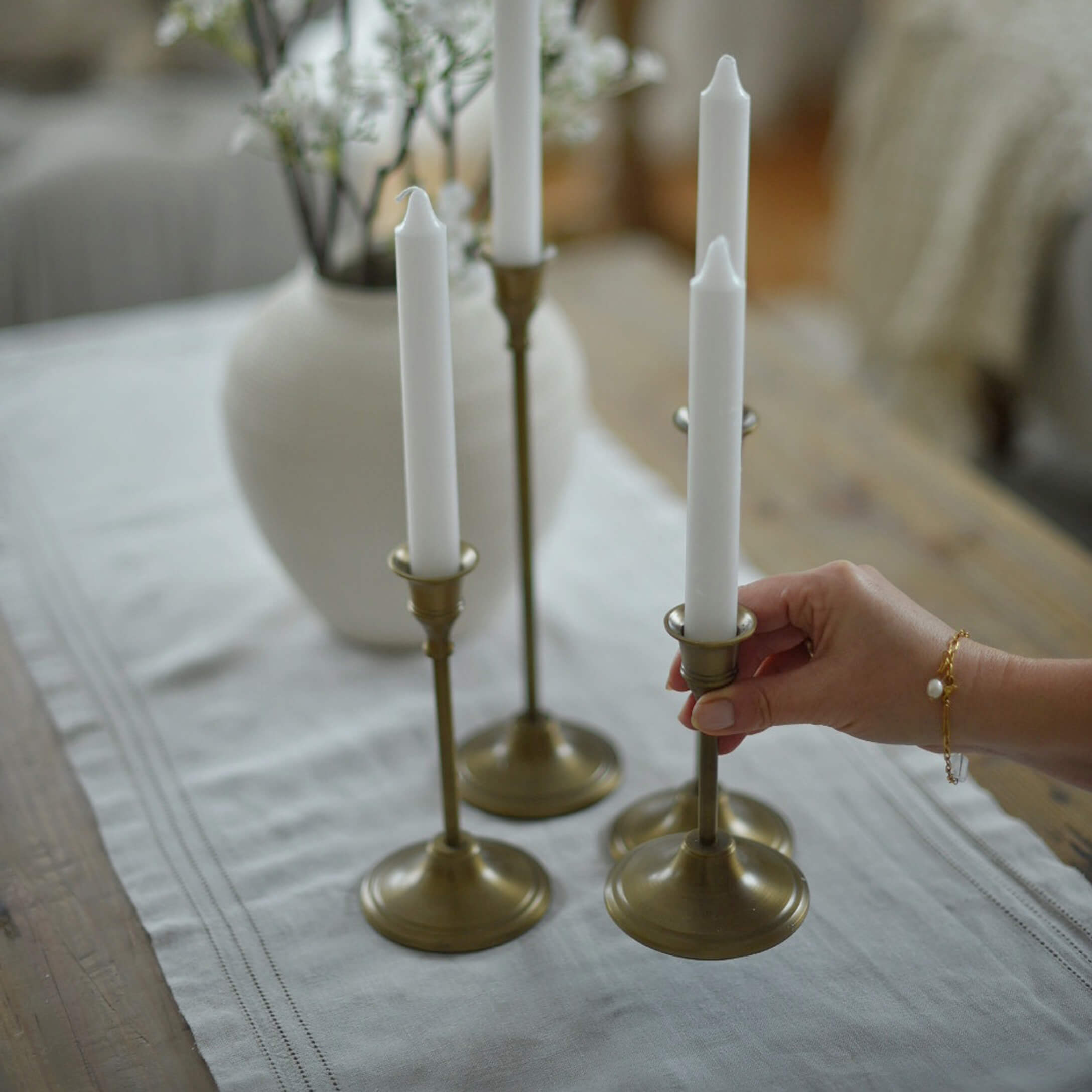 Set di quattro candelabri in ottone con candele bianche su tovaglia di lino in ambiente accogliente