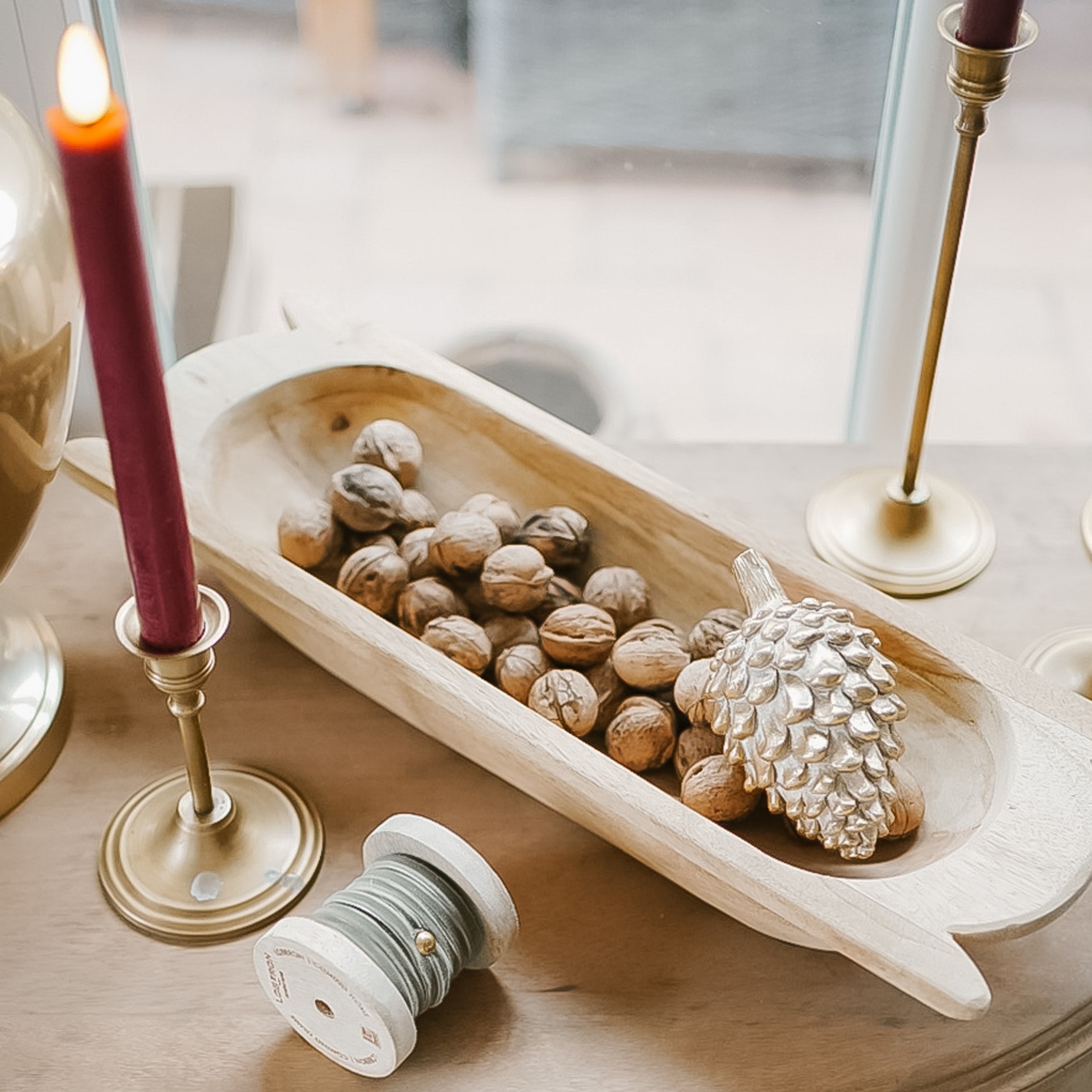 Ciotola in legno con noci e pigna dorata su tavolo con candelabri in ottone