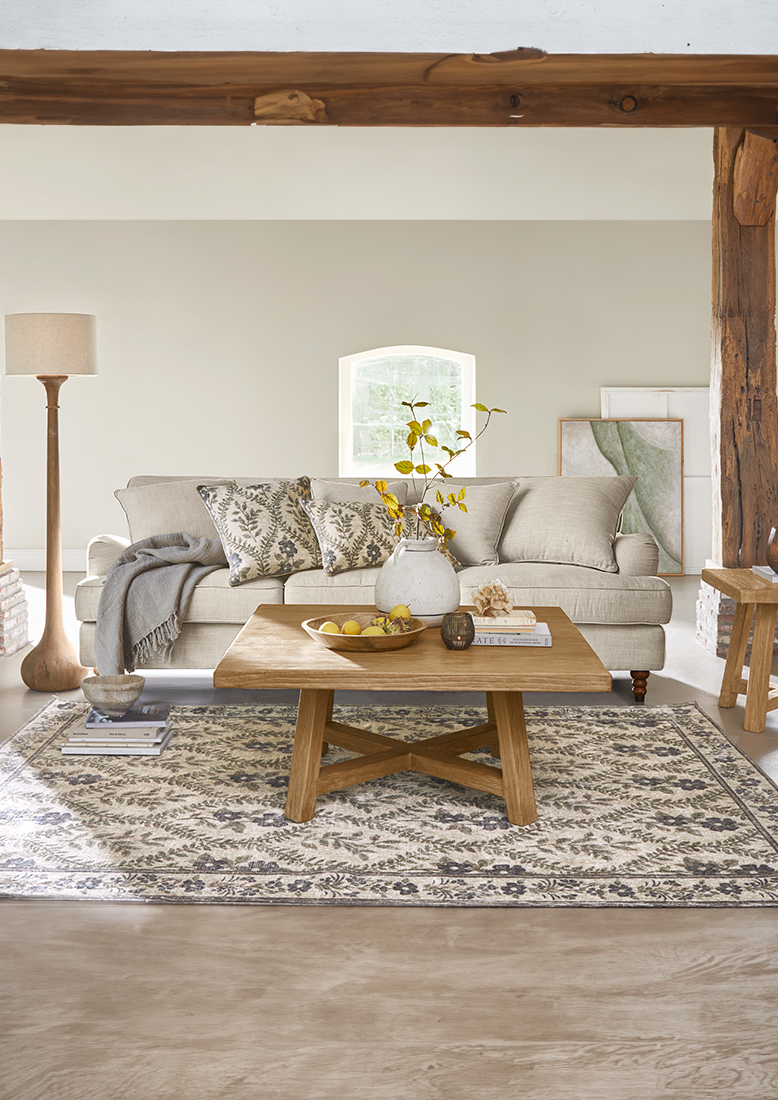 Divano beige in tessuto con cuscini decorativi e tavolino in legno su tappeto a motivi in soggiorno luminoso