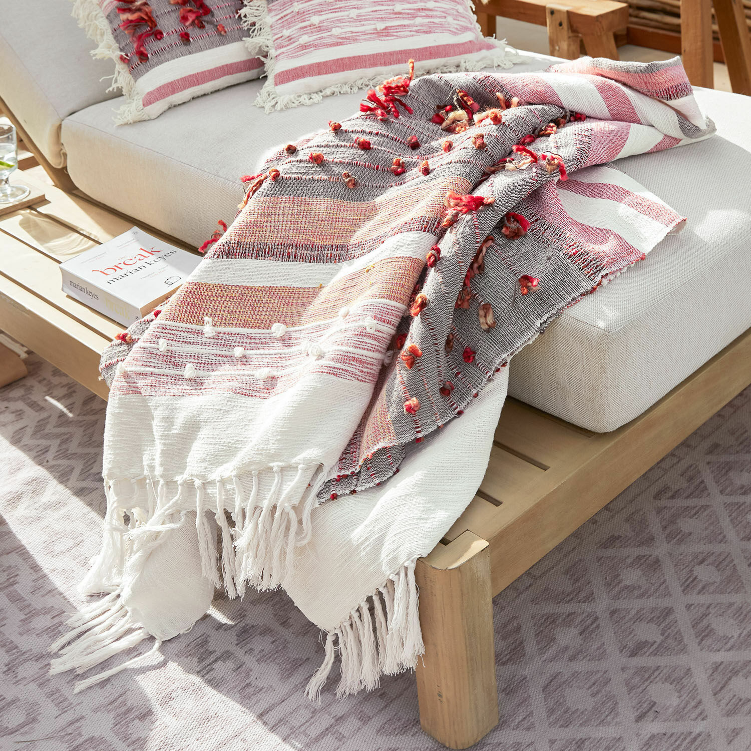 Plaid Yazmira Plaid decorativo a righe rosse e bianche con frange su divano grigio chiaro con struttura in legno