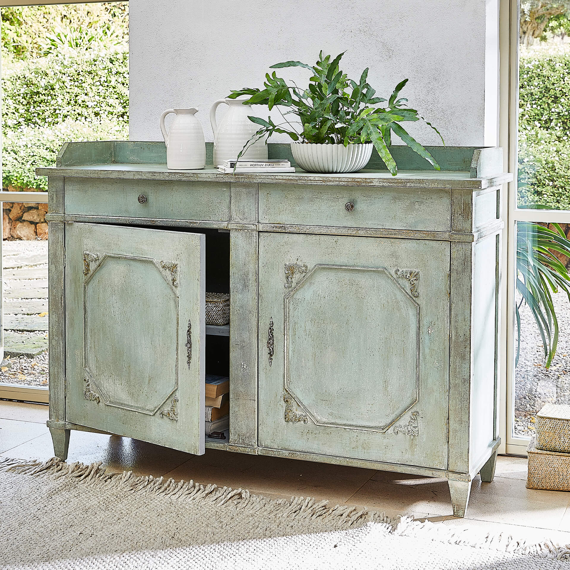 Credenza verde in legno con due cassetti e ante decorative in soggiorno luminoso