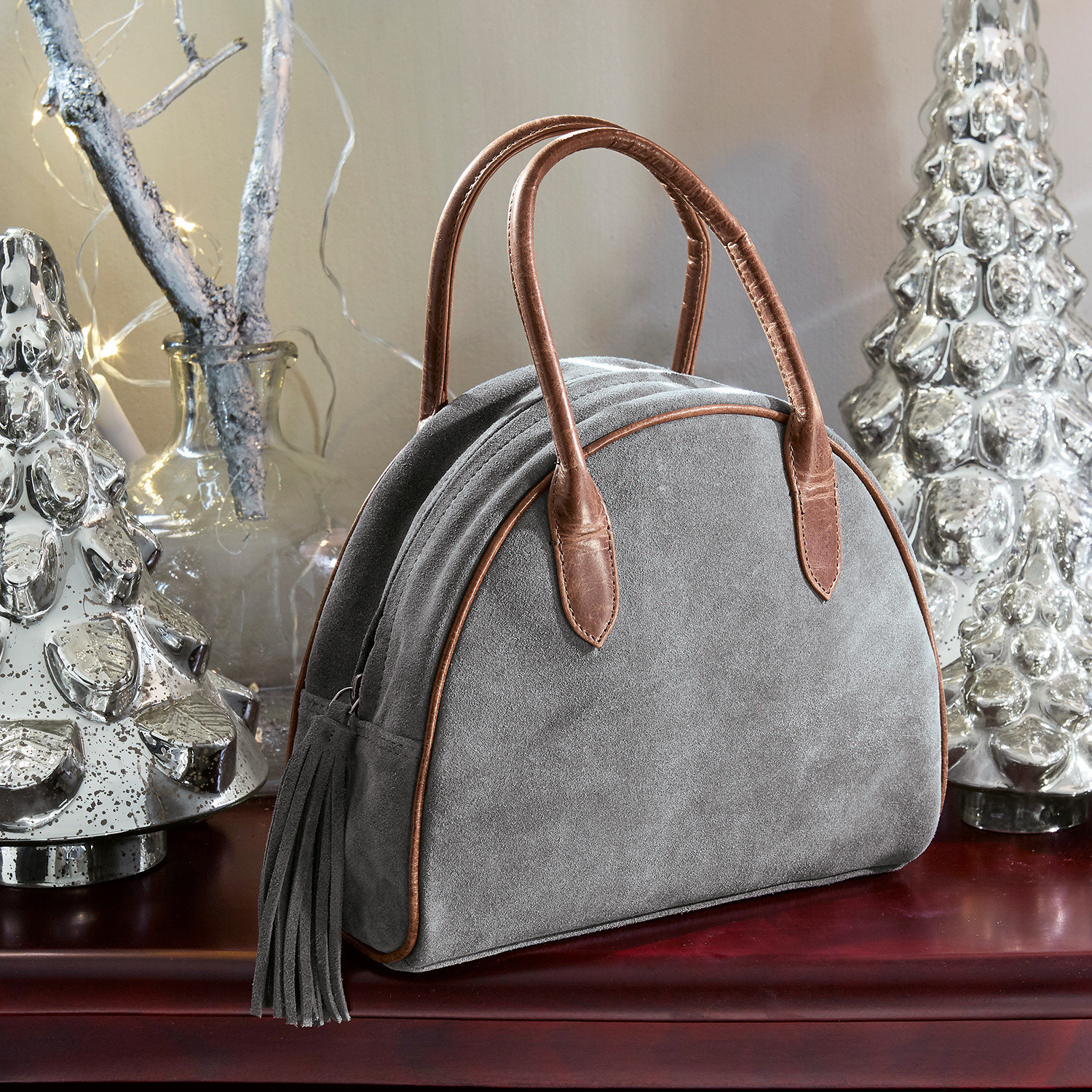 Borsa Elisabeta Borsa in camoscio grigia con manici in pelle marrone e nappine su tavolo con decorazioni natalizie