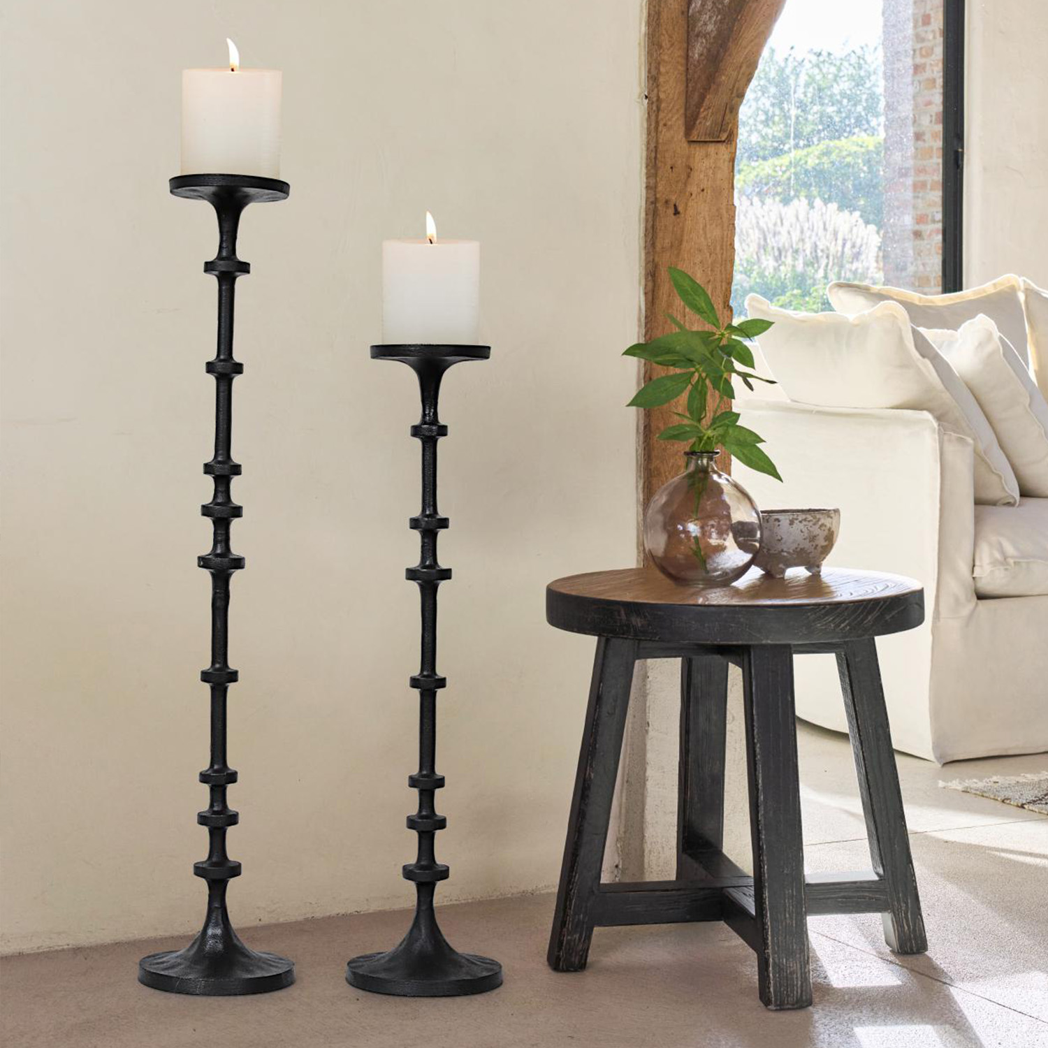 Due candelabri in metallo nero con candele bianche accanto a uno sgabello in legno e un divano in soggiorno