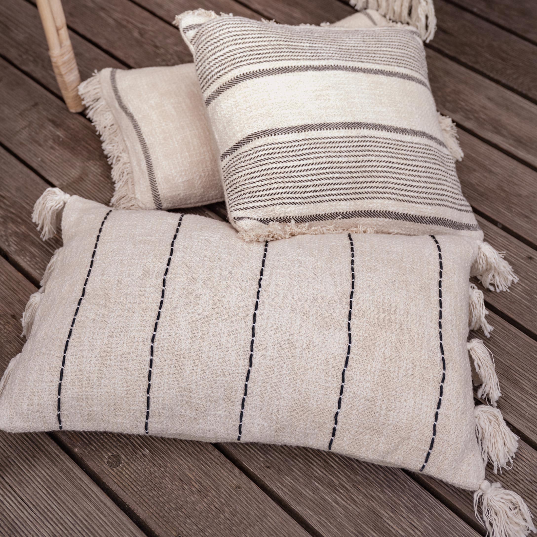 Set di tre cuscini decorativi in cotone crema con motivi neri e marroni su pavimento in legno