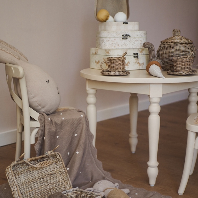 Tavolo beige con set da tè in vimini e scatole decorative in una cameretta accogliente
