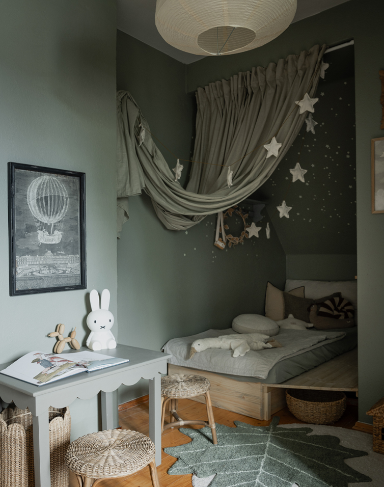 Camera per bambini accogliente con pareti verdi, letto basso e decorazioni a stelle sospese per un'atmosfera rilassante