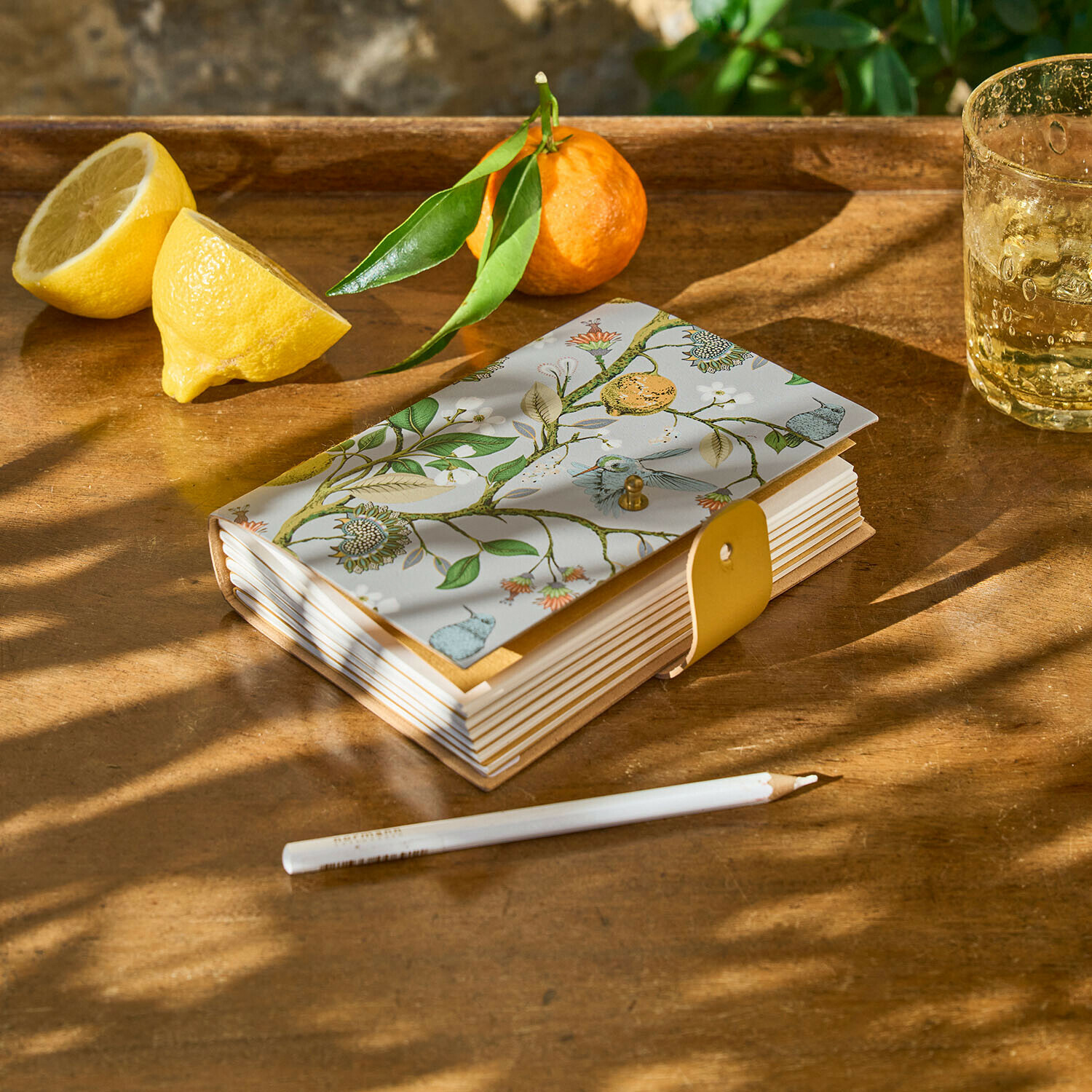 Taccuino Ambroisea Taccuino con copertina decorativa a motivo vegetale e chiusura gialla su tavolo in legno con limone e mandarino