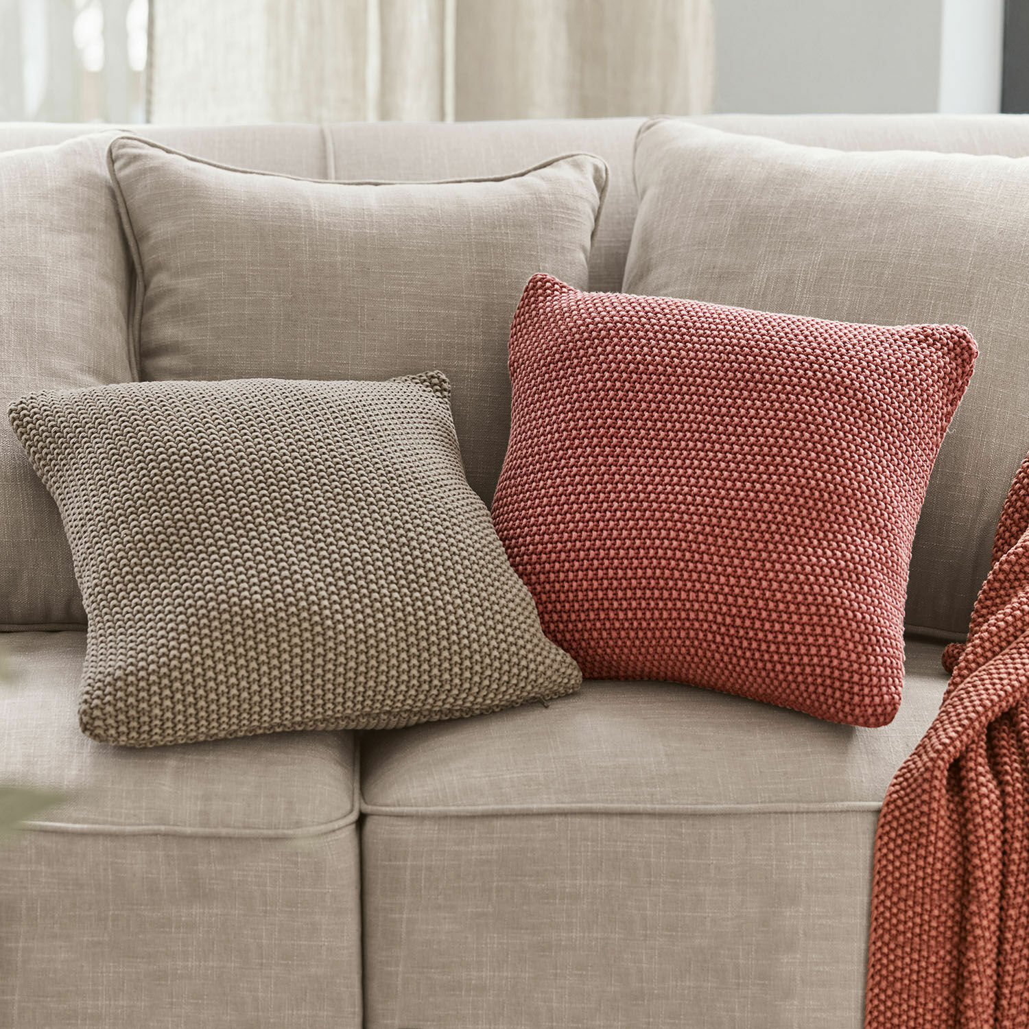 Coppia di copricuscini Terry Due cuscini quadrati in maglia beige e mattone su divano grigio chiaro per arredamento