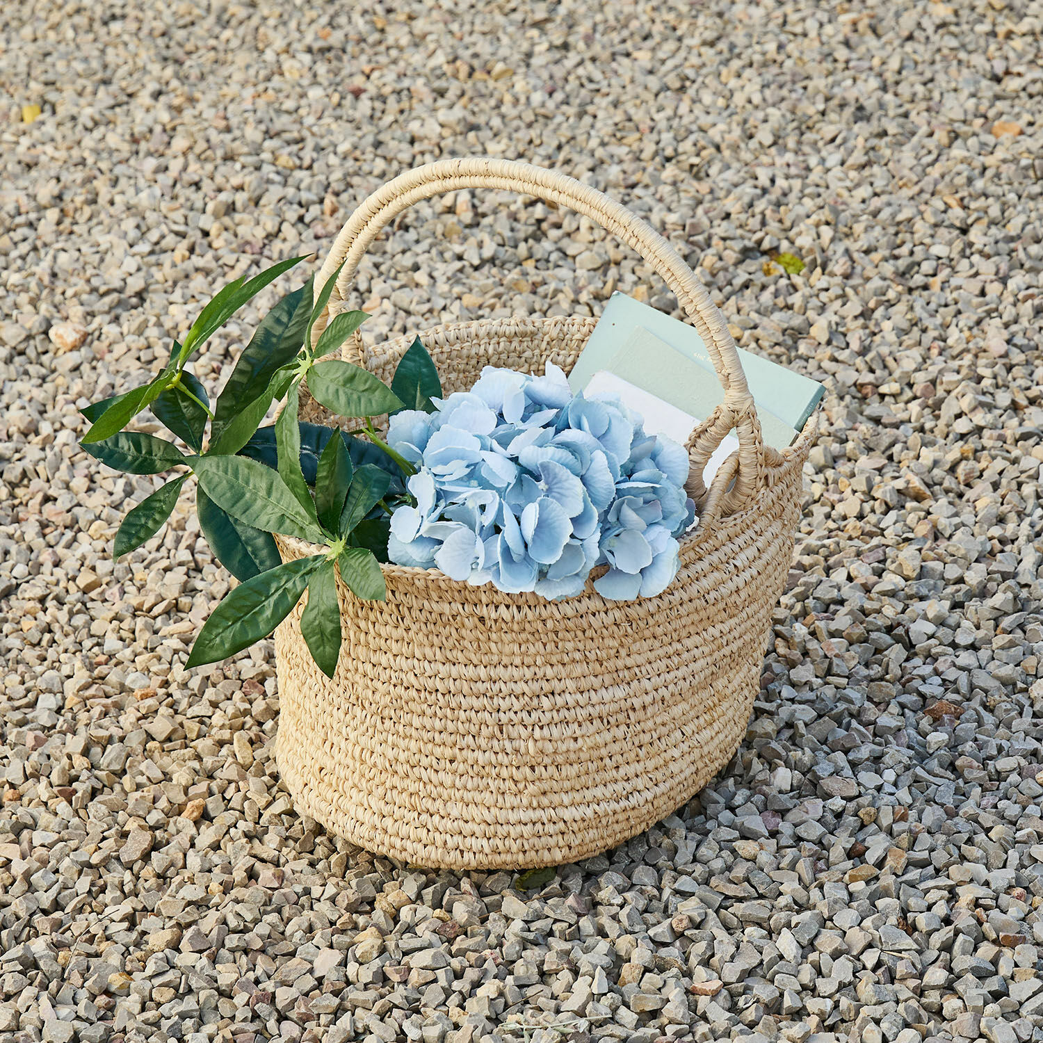 Cestino Shanoura Cesto intrecciato naturale in erba marina con fiori azzurri e foglie verdi su ciottoli