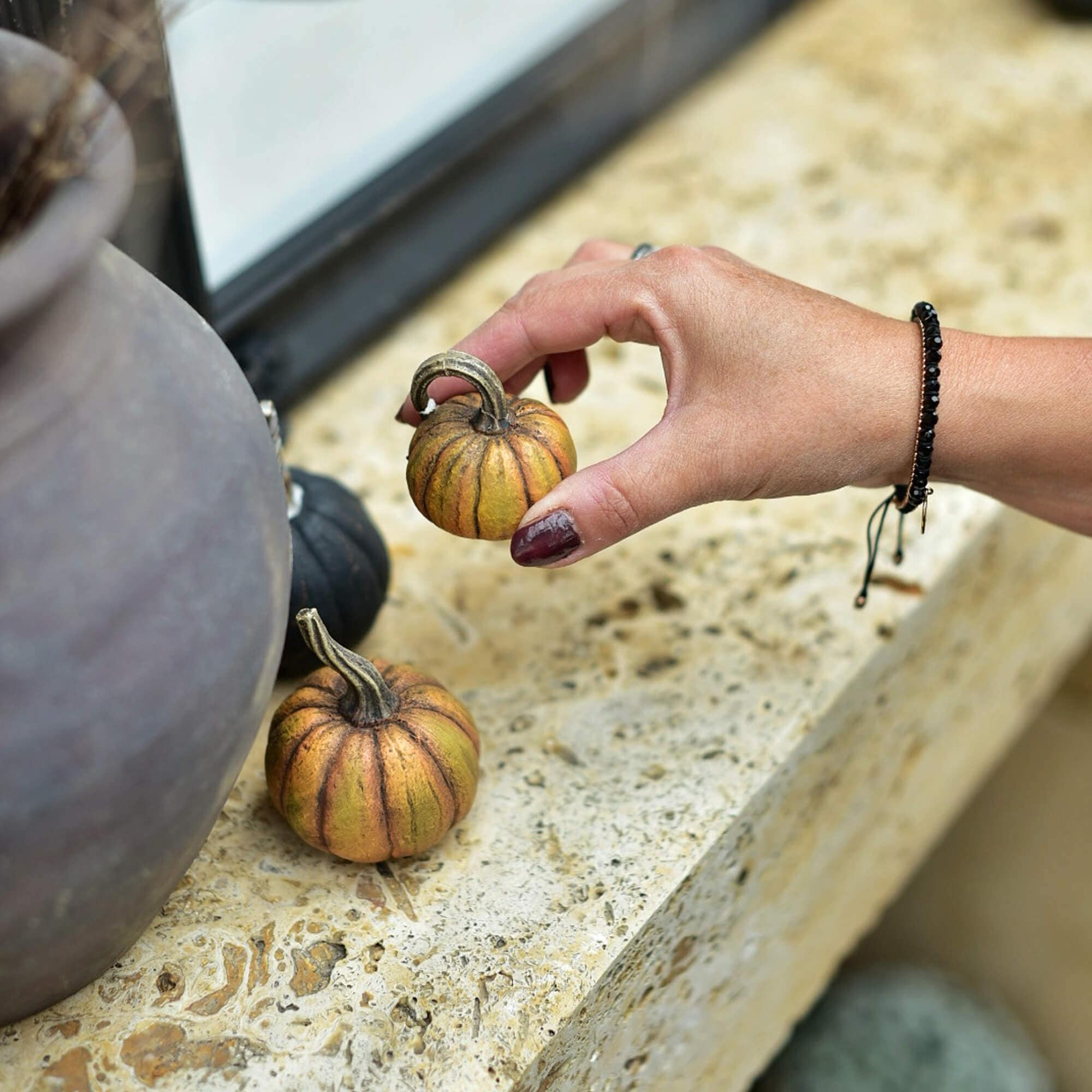 Mano che tiene una piccola zucca decorativa arancione-marrone su una superficie in pietra