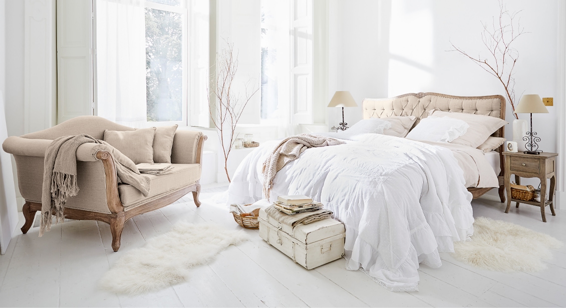 Camera da letto accogliente con letto imbottito beige e divano vintage su pavimento in legno chiaro