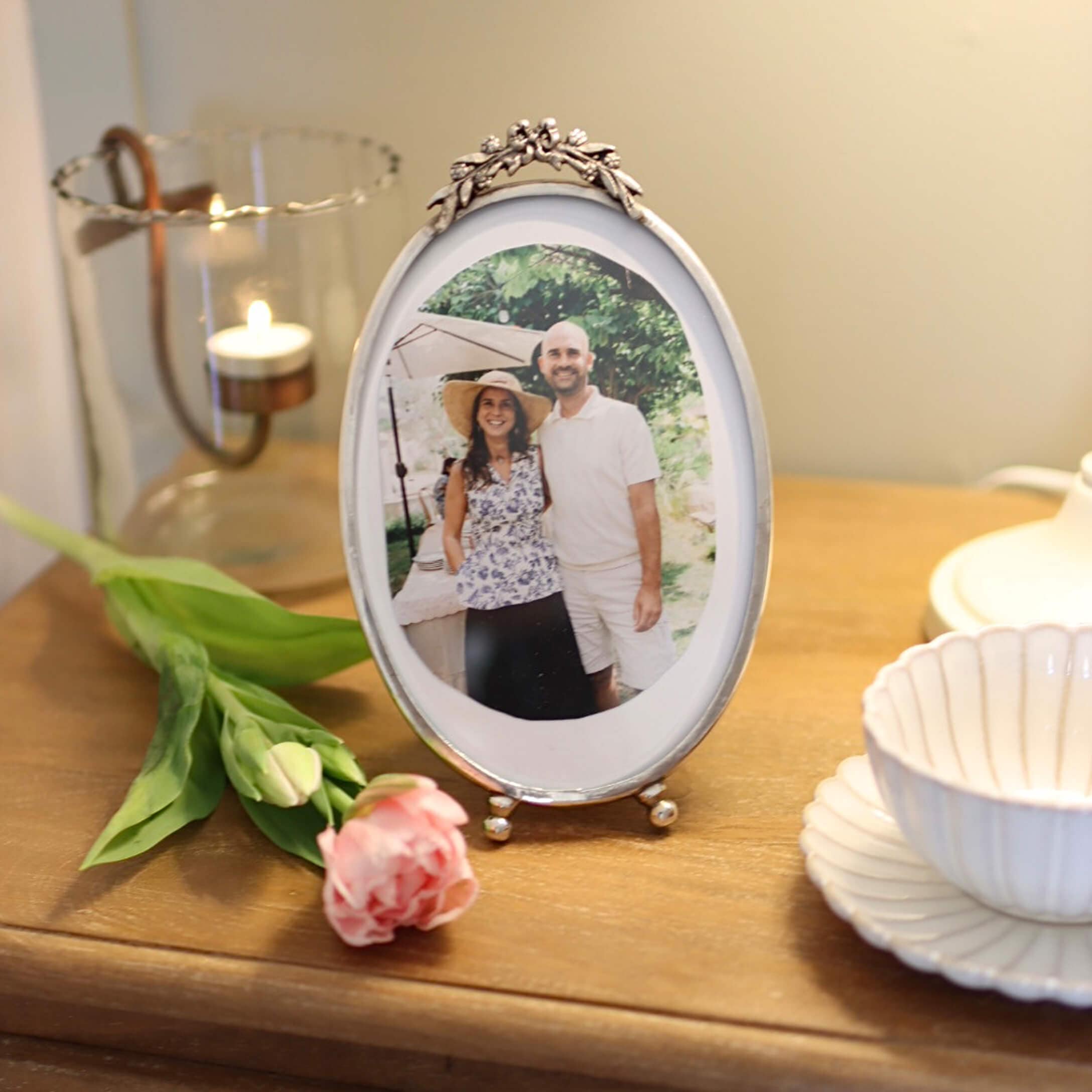 Cornice fotografica ovale in argento con decorazione floreale su tavolo in legno con rosa e portacandela