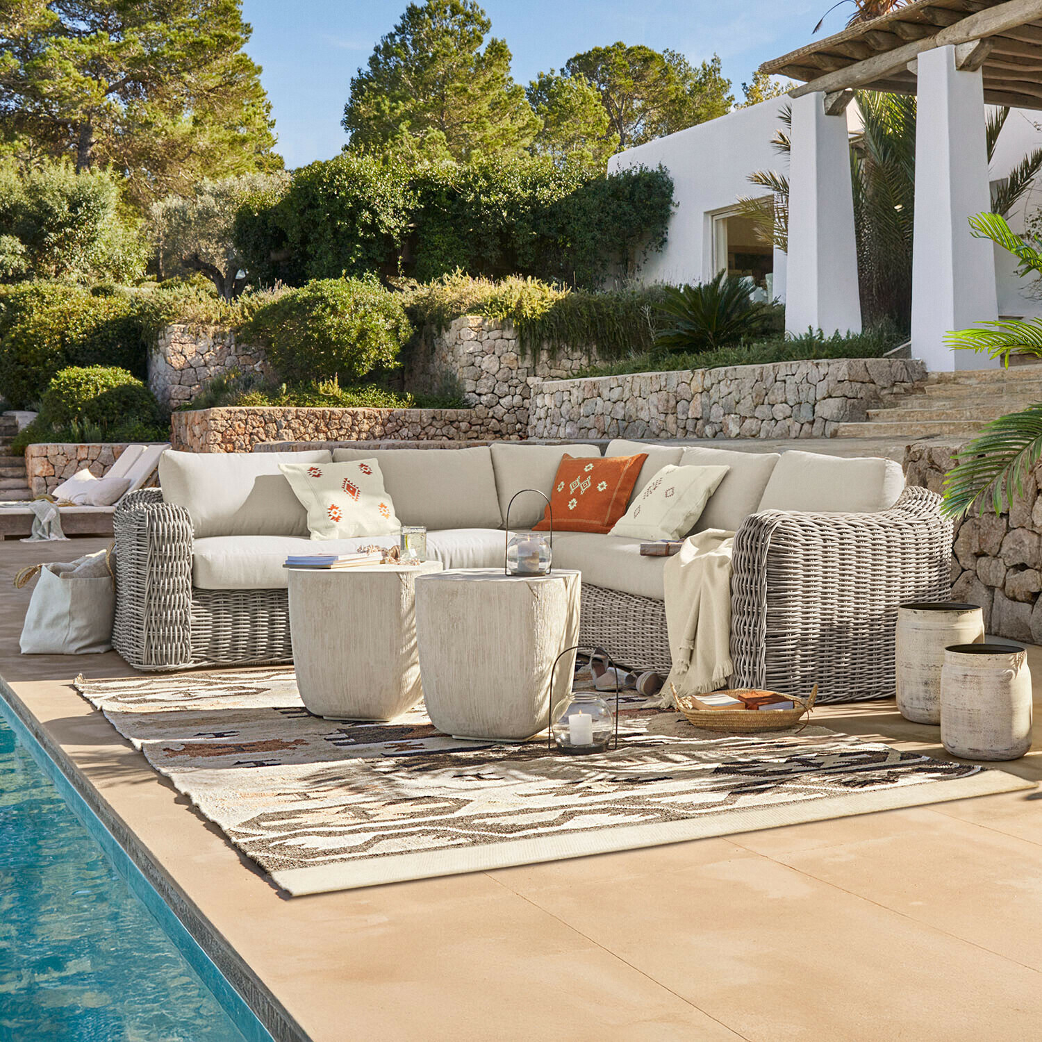 Set di mobili da giardino con divano in rattan beige e cuscini decorativi vicino alla piscina