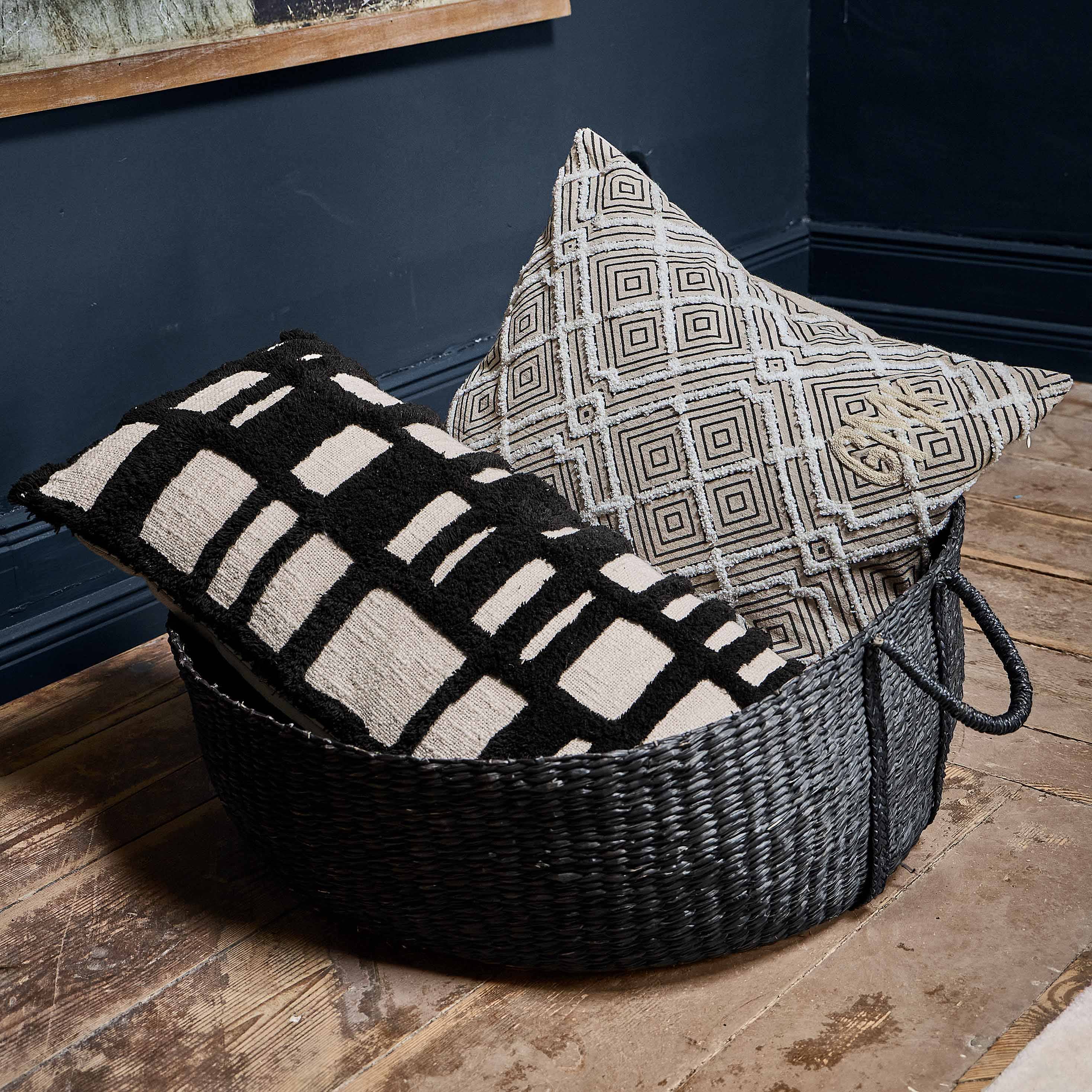 Cuscino decorativo bianco e nero con motivo geometrico in cesta su pavimento in legno